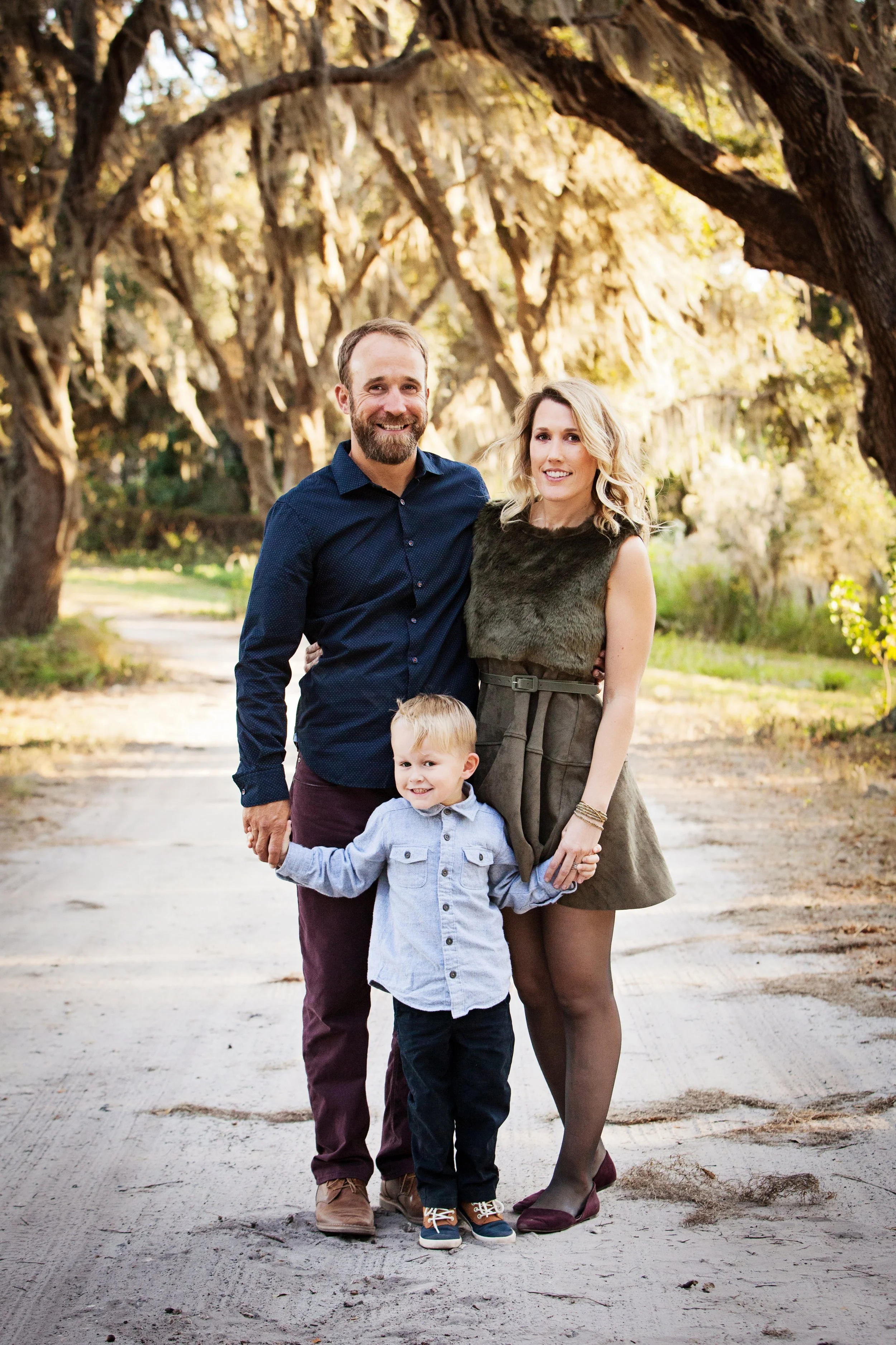 Outdoor family photography of parents and young son holding hands on a tree-lined path in autumn in Florida.