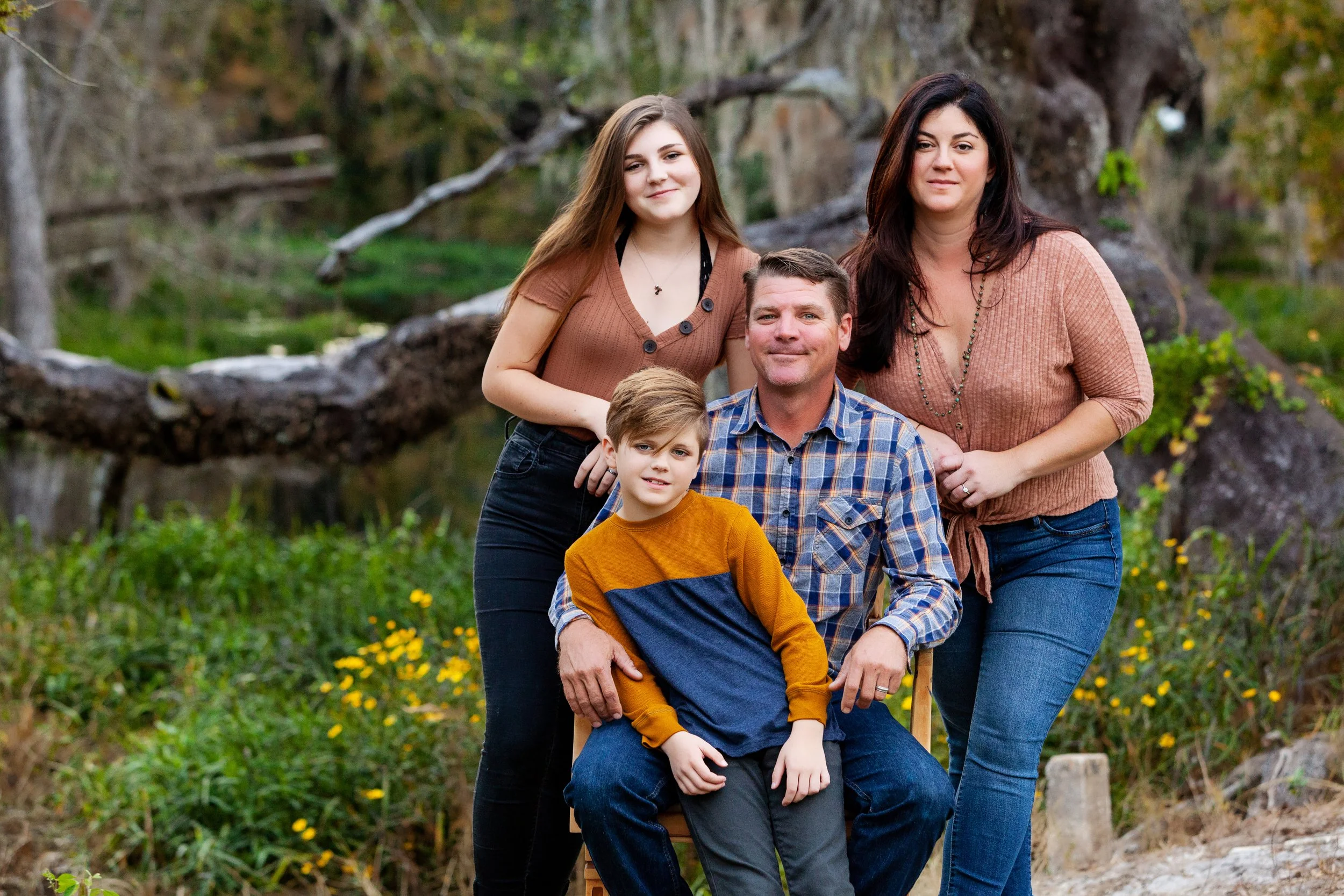Outdoor family portrait of parents and two children surrounded by trees and yellow wildflowers