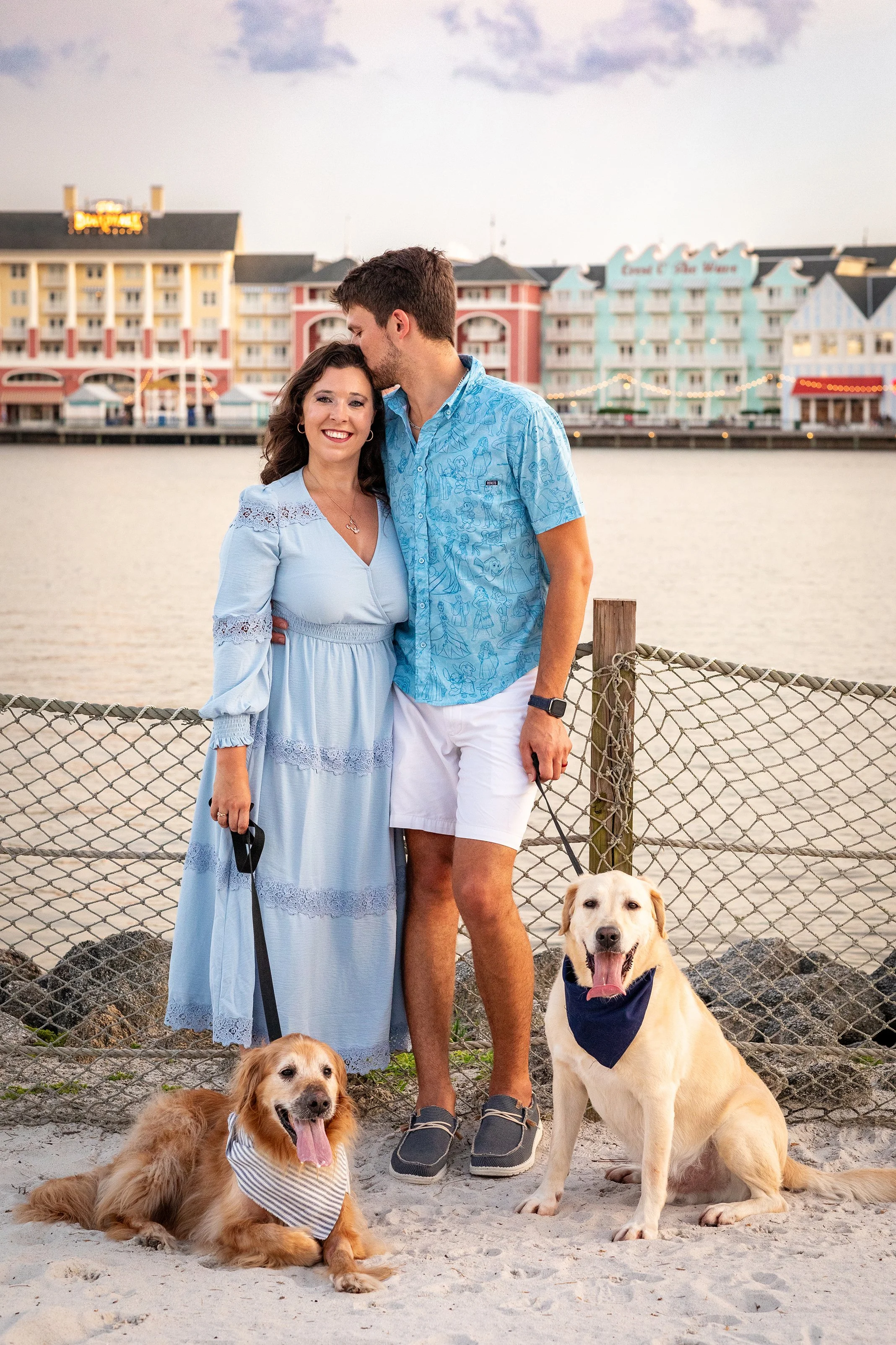 Lifestyle couple photography of a couple standing on the beach with their dogs at sunset