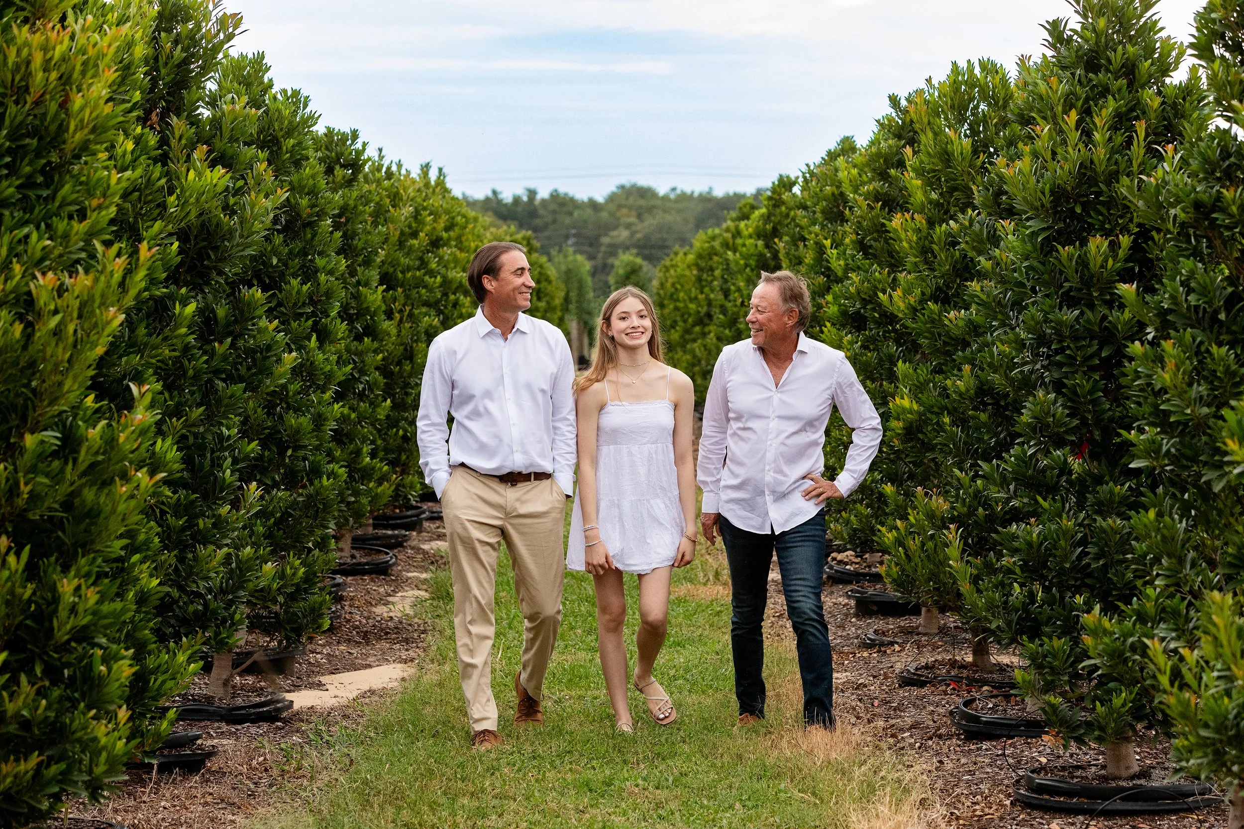 Lifestyle group photography of three people walking and talking through a garden path with lush green plants on either side.