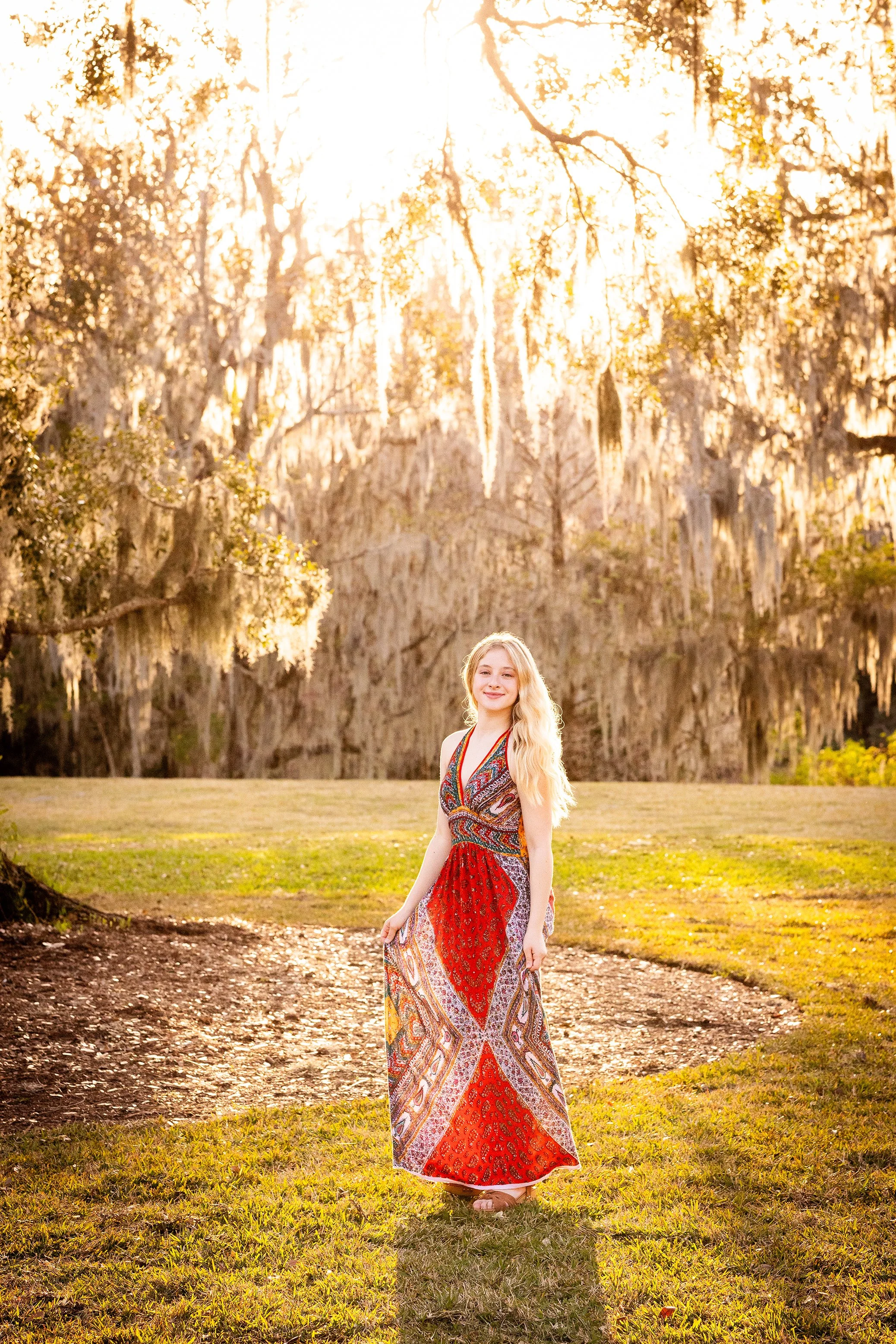 Outdoor lifestyle portrait of a woman in a colorful dress standing beneath moss-covered trees at sunset, photographed by Lindsay Parks Photography