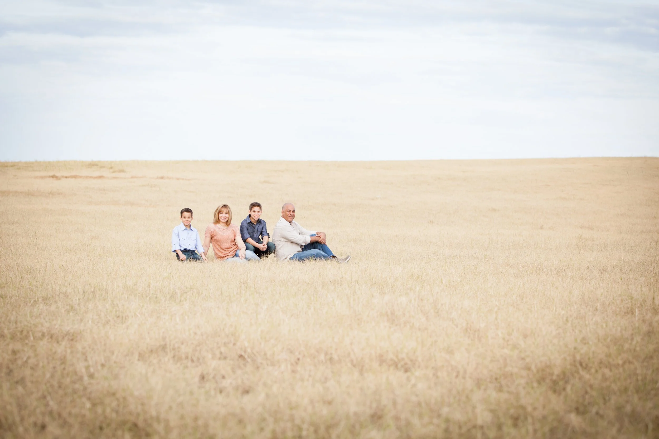 Outdoor family photography of a family of four sitting together in a golden grass field