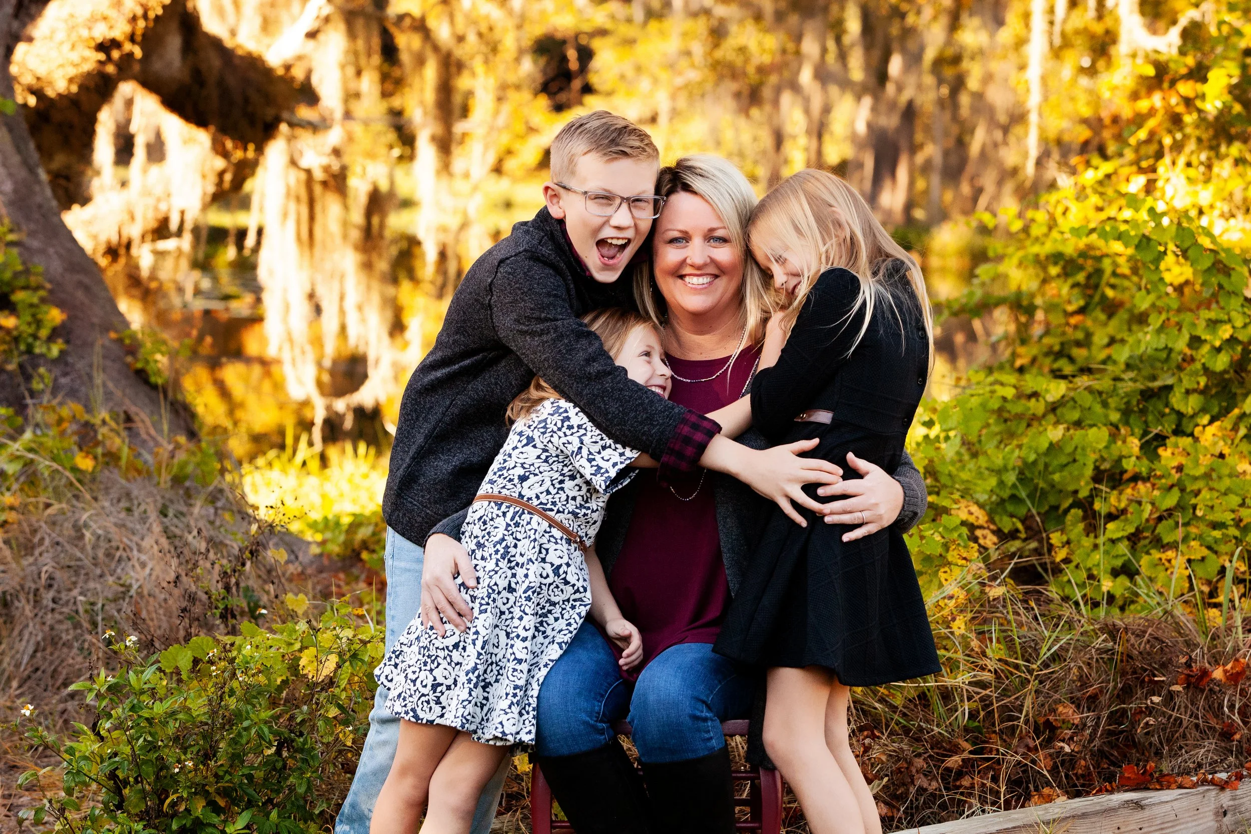 Fall family photography of a mother and three children hugging and smiling outdoors during golden hour. 