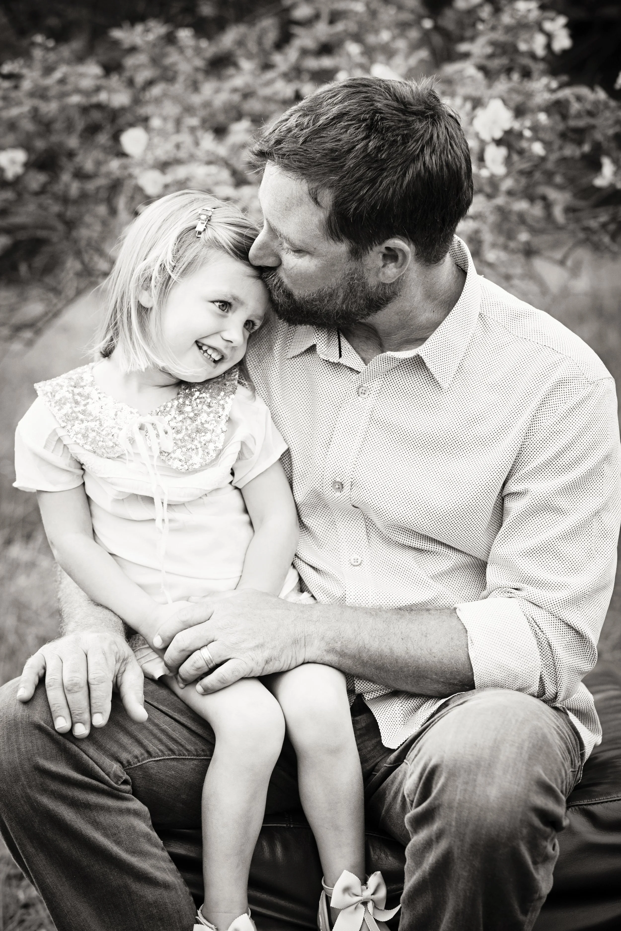 Tender father-daughter lifestyle portrait of a man kissing his daughter’s forehead on a park bench