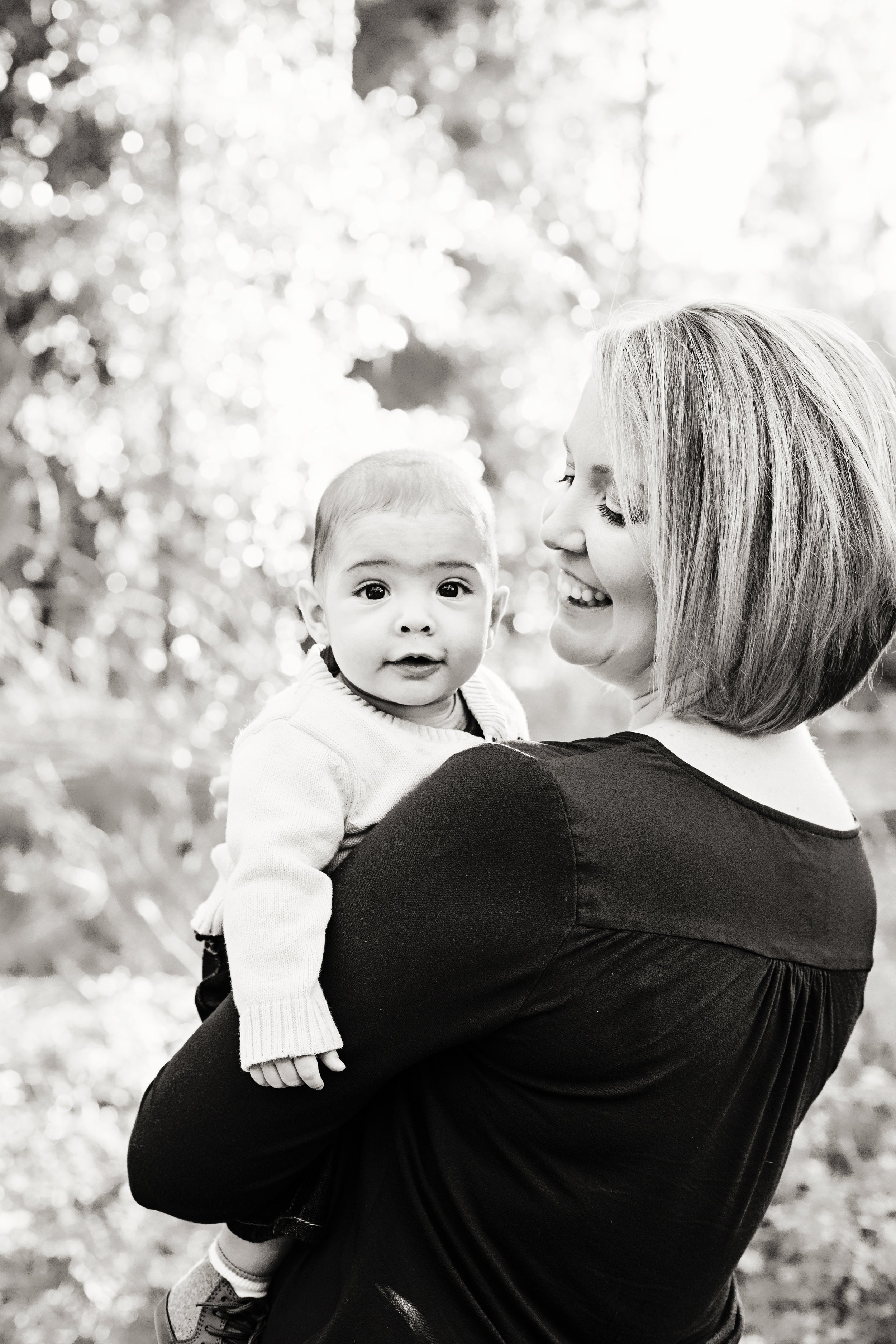 Black and white newborn portrait of a mother holding her baby outdoors beneath trees