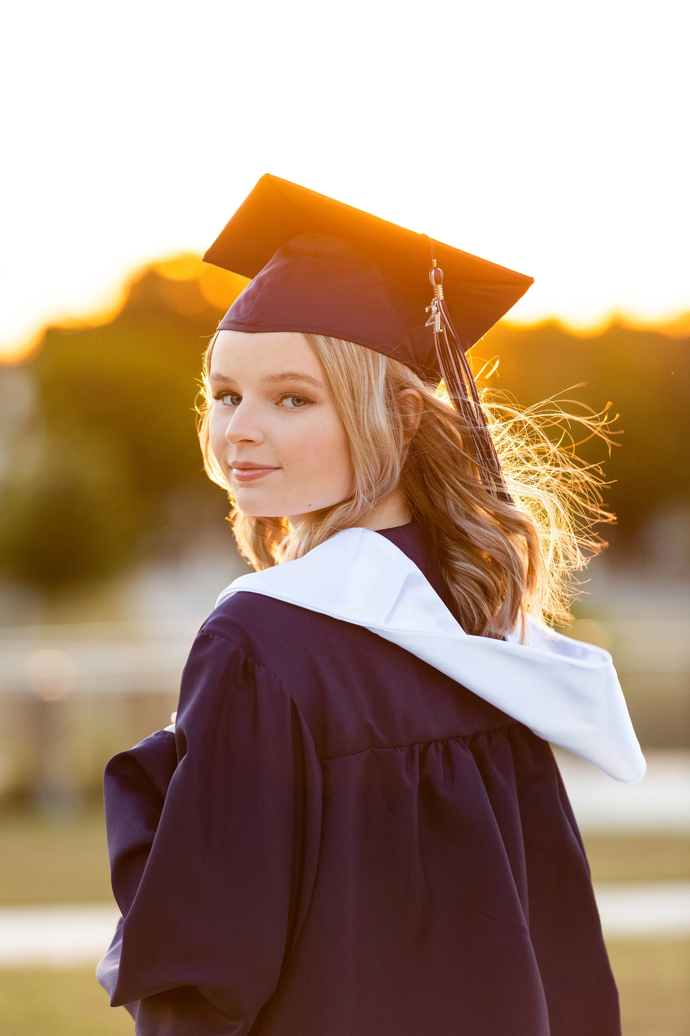 Senior graduation portrait of a young woman in cap and gown during golden hour, photographed by Lindsay Parks Photography