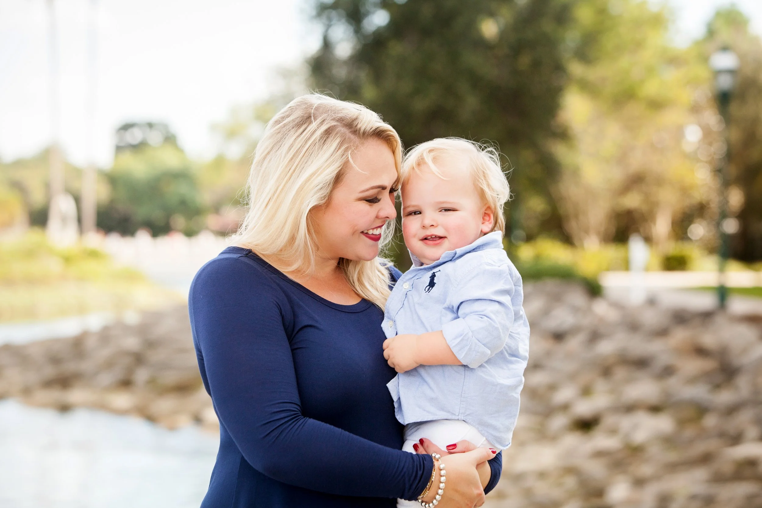 Lifestyle family photography of a mother holding her child near a river in a park setting