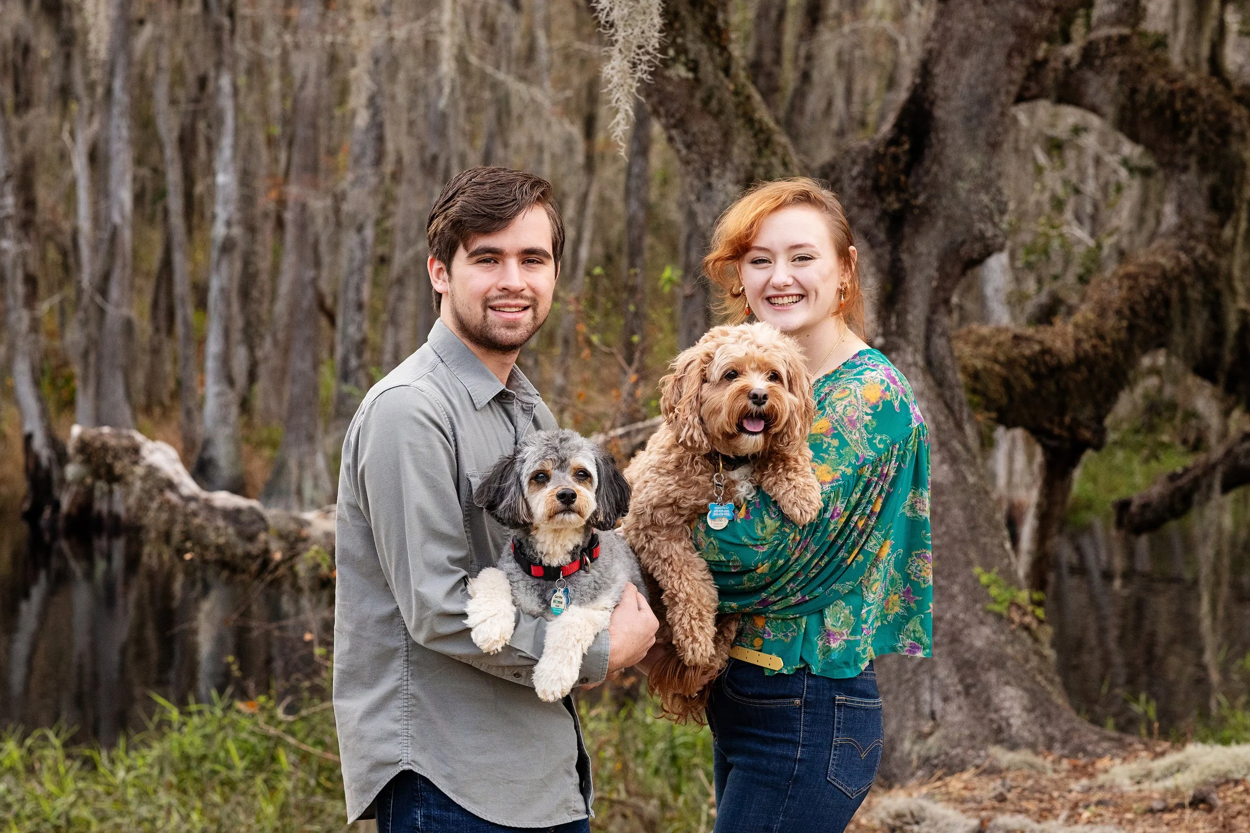 Lifestyle couple photography of a smiling couple holding their dogs in a wooded setting