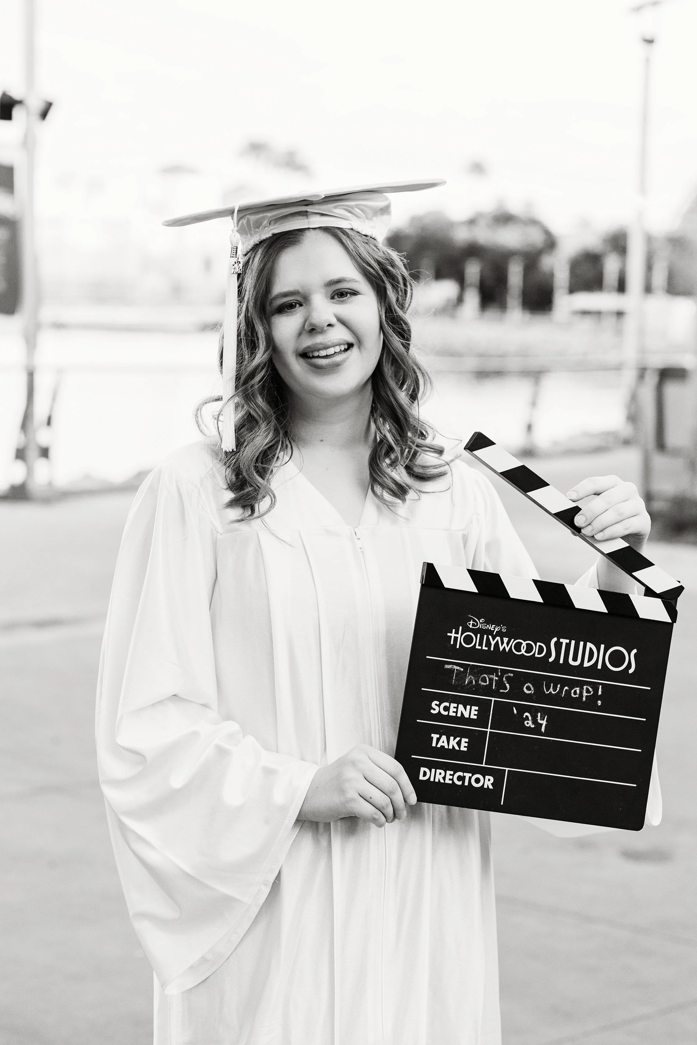 Creative graduation photography of a graduate holding a film clapperboard near water, photographed by Lindsay Parks Photography