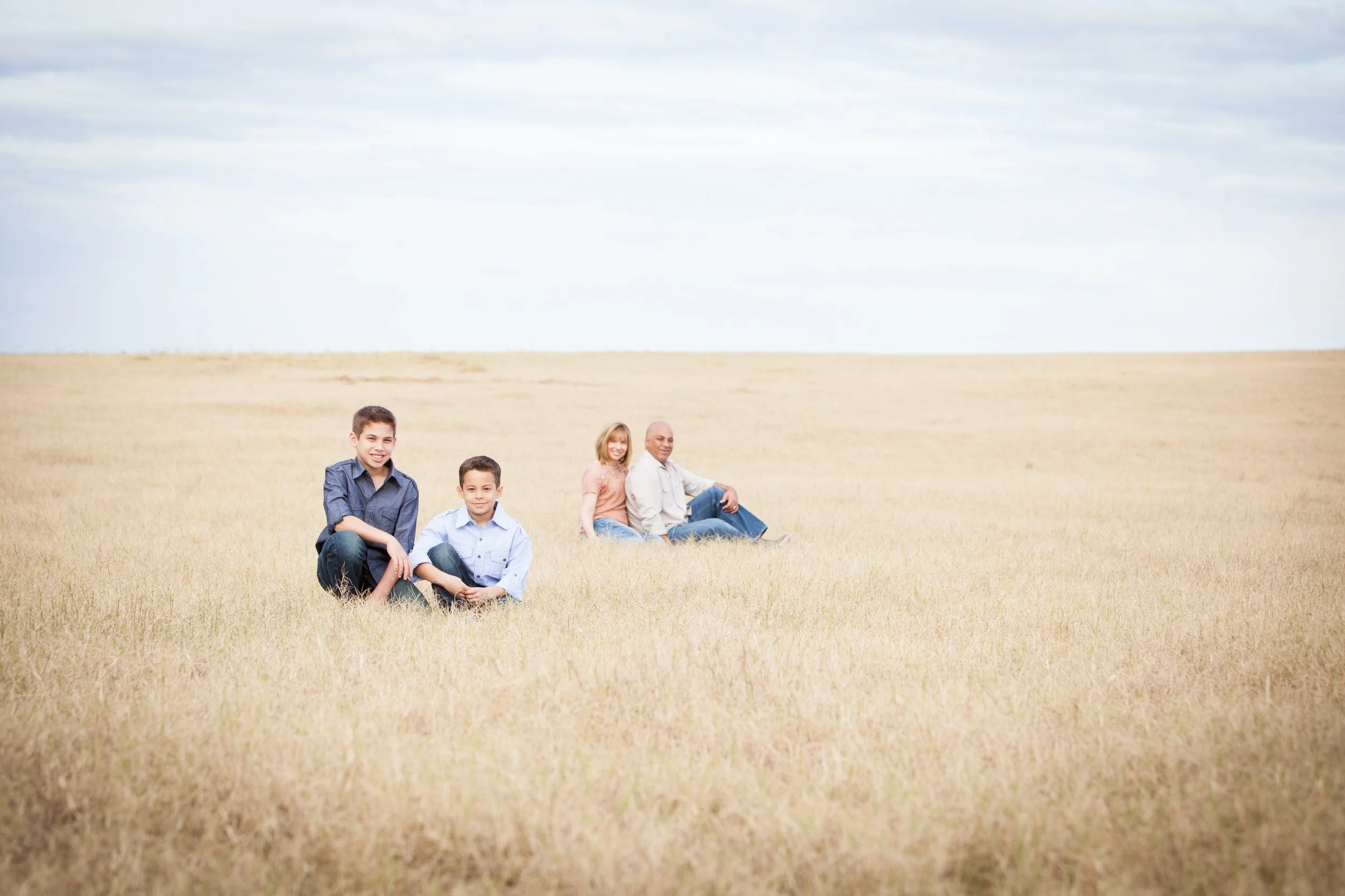 Lifestyle family session of two children sitting in a grassy field with parents behind them