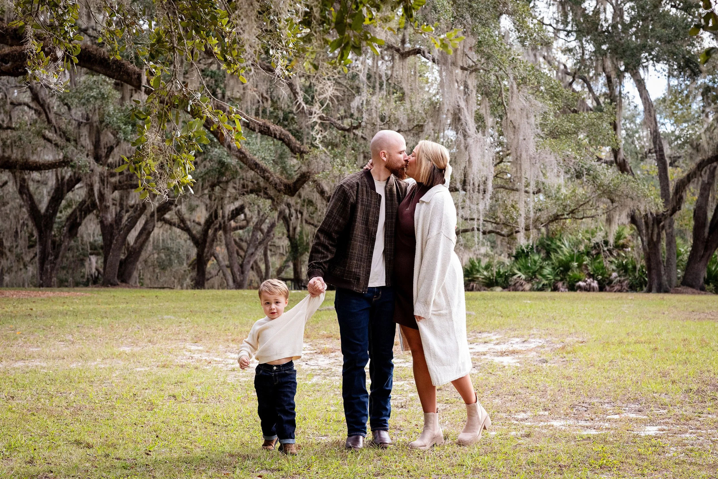 Lifestyle family portrait of parents sharing a kiss while holding hands with their young son. 