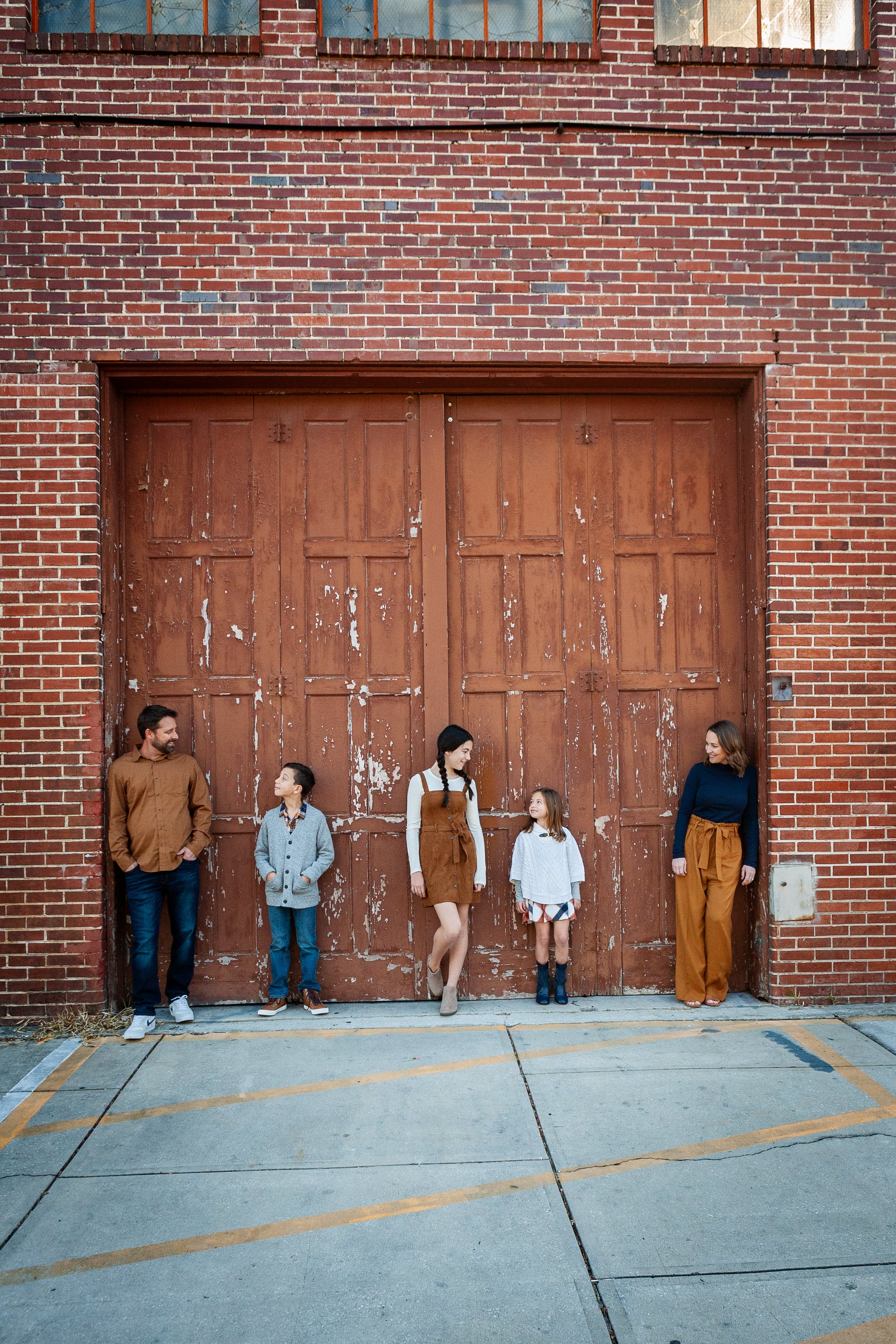 Urban family portrait of a family of five standing in front of a weathered wooden door and brick wall