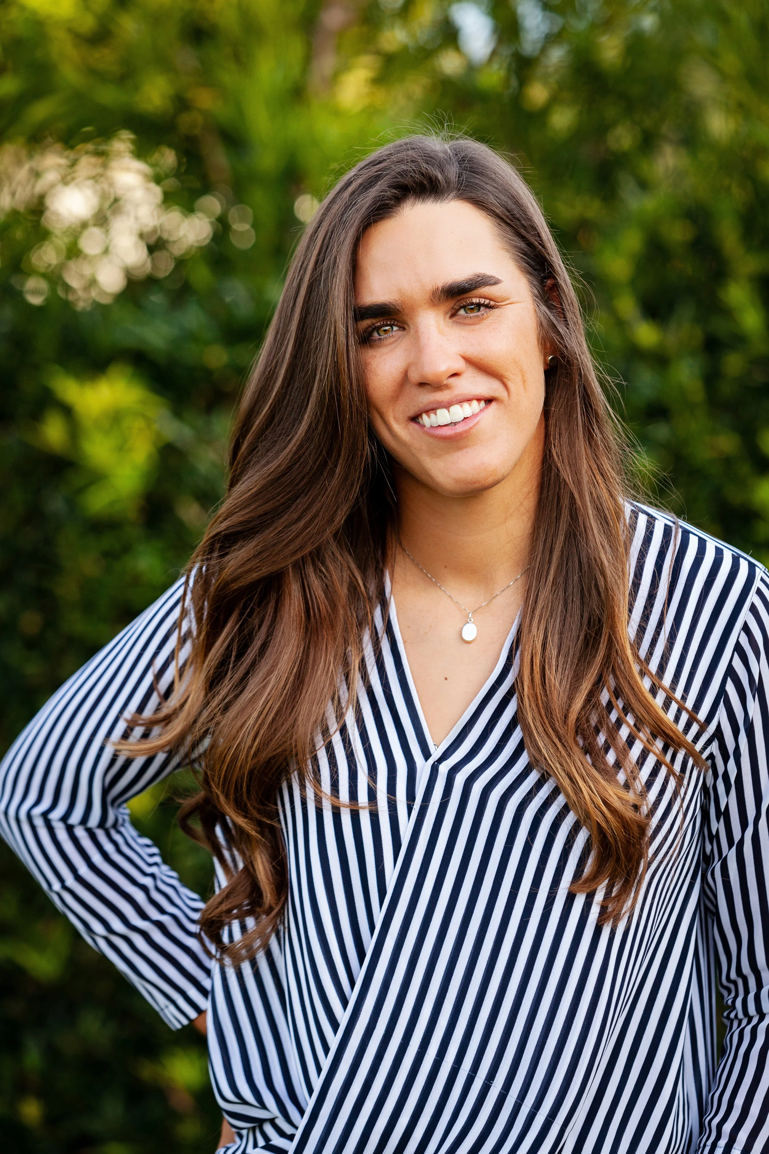 Outdoor lifestyle portrait of a woman smiling in front of lush green foliage