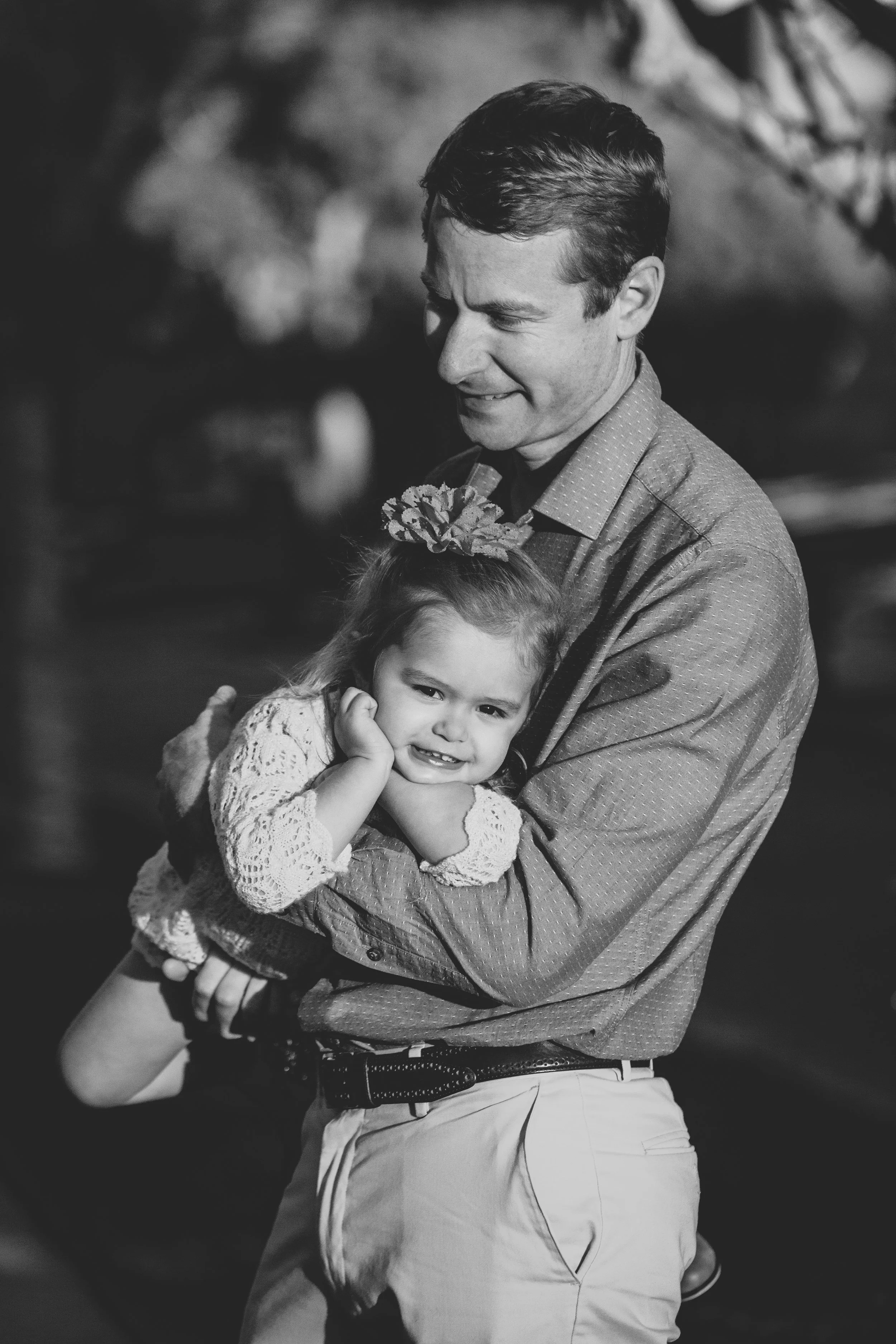 Lifestyle family portrait of a father holding his smiling daughter beneath trees