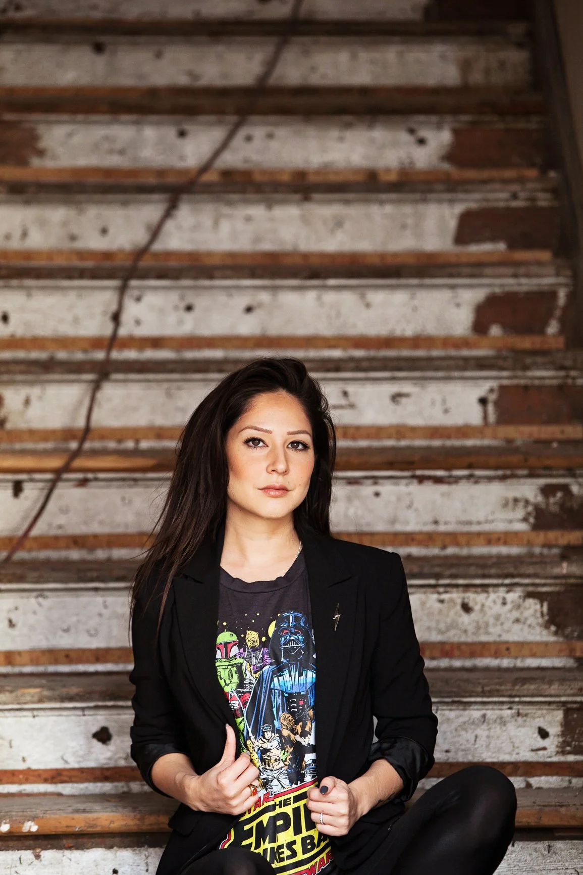 Personal branding portrait of a woman seated on wooden stairs wearing a blazer and graphic t-shirt with stunning natural light.