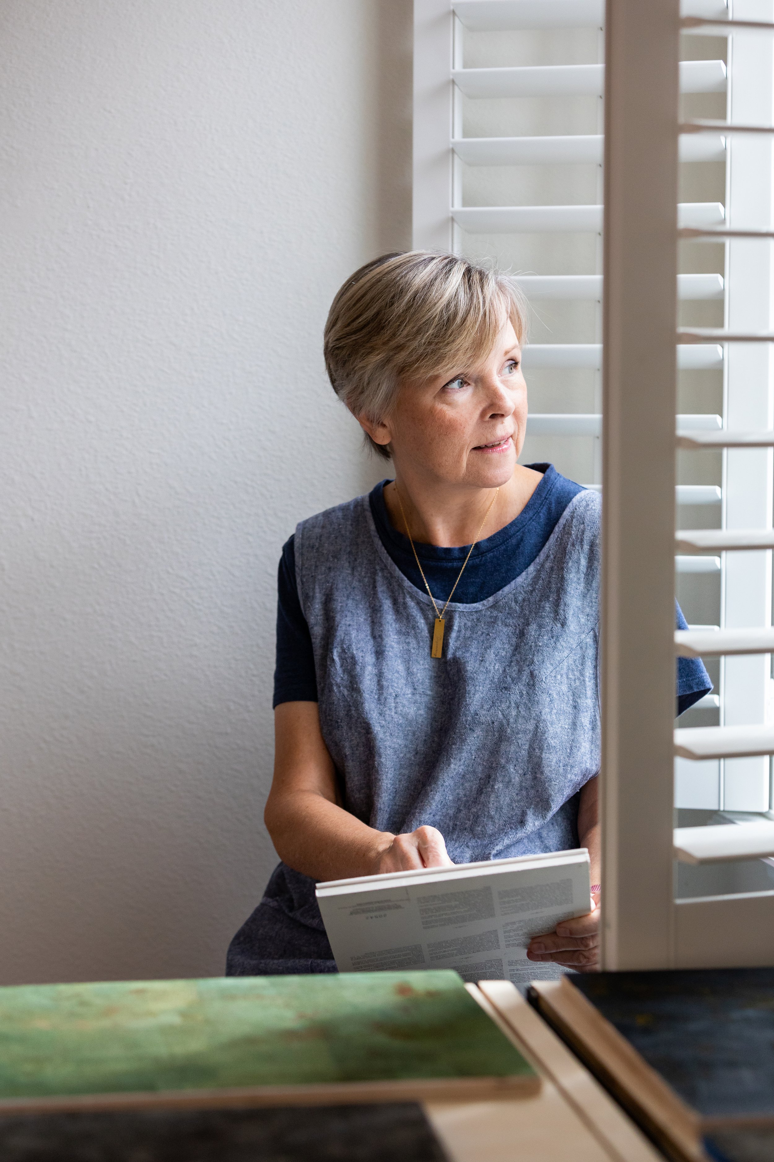 Lifestyle portrait of a woman looking out a window while holding a newspaper