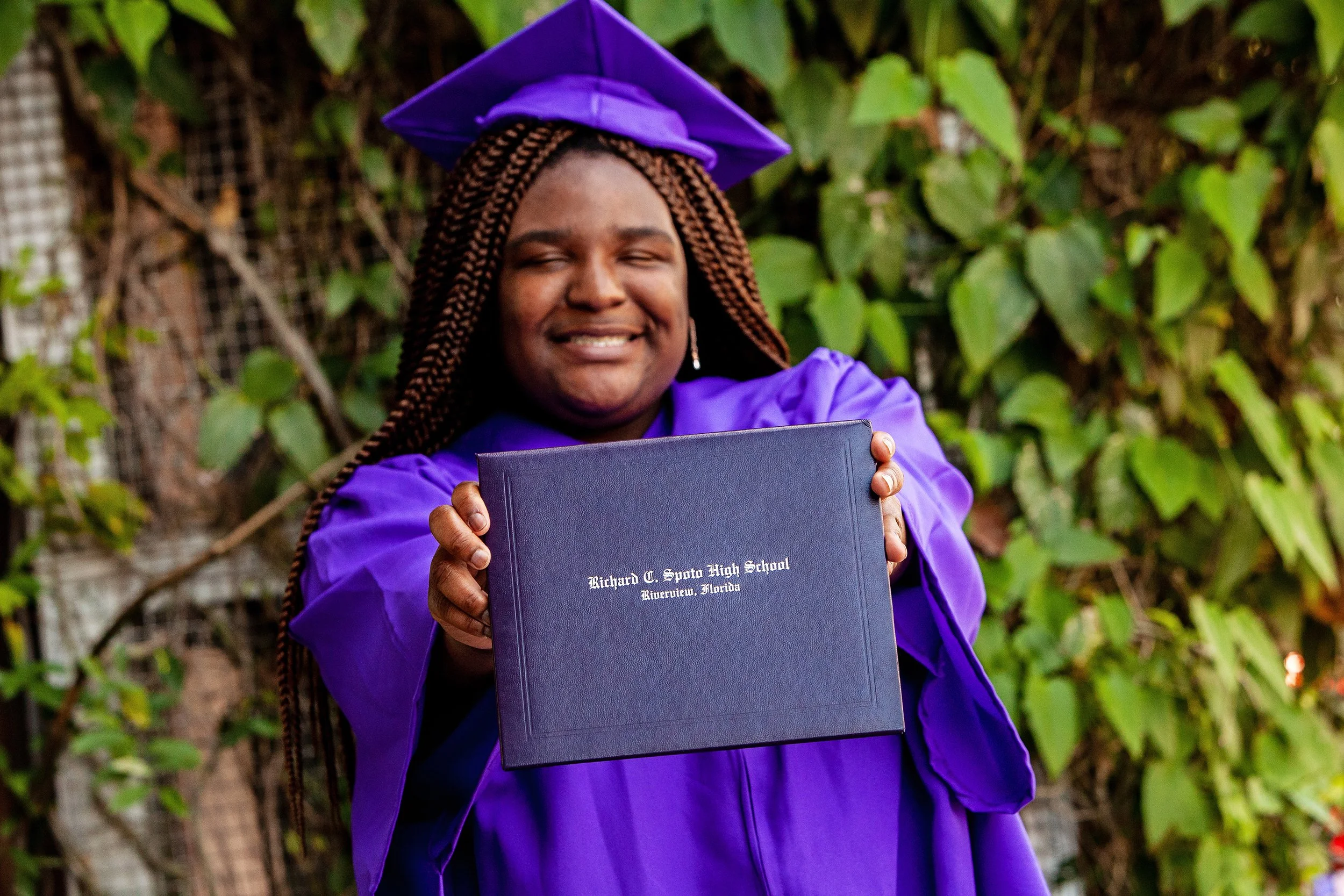 Graduation portrait of a senior holding her diploma with eyes closed in celebration, photographed by Lindsay Parks Photography