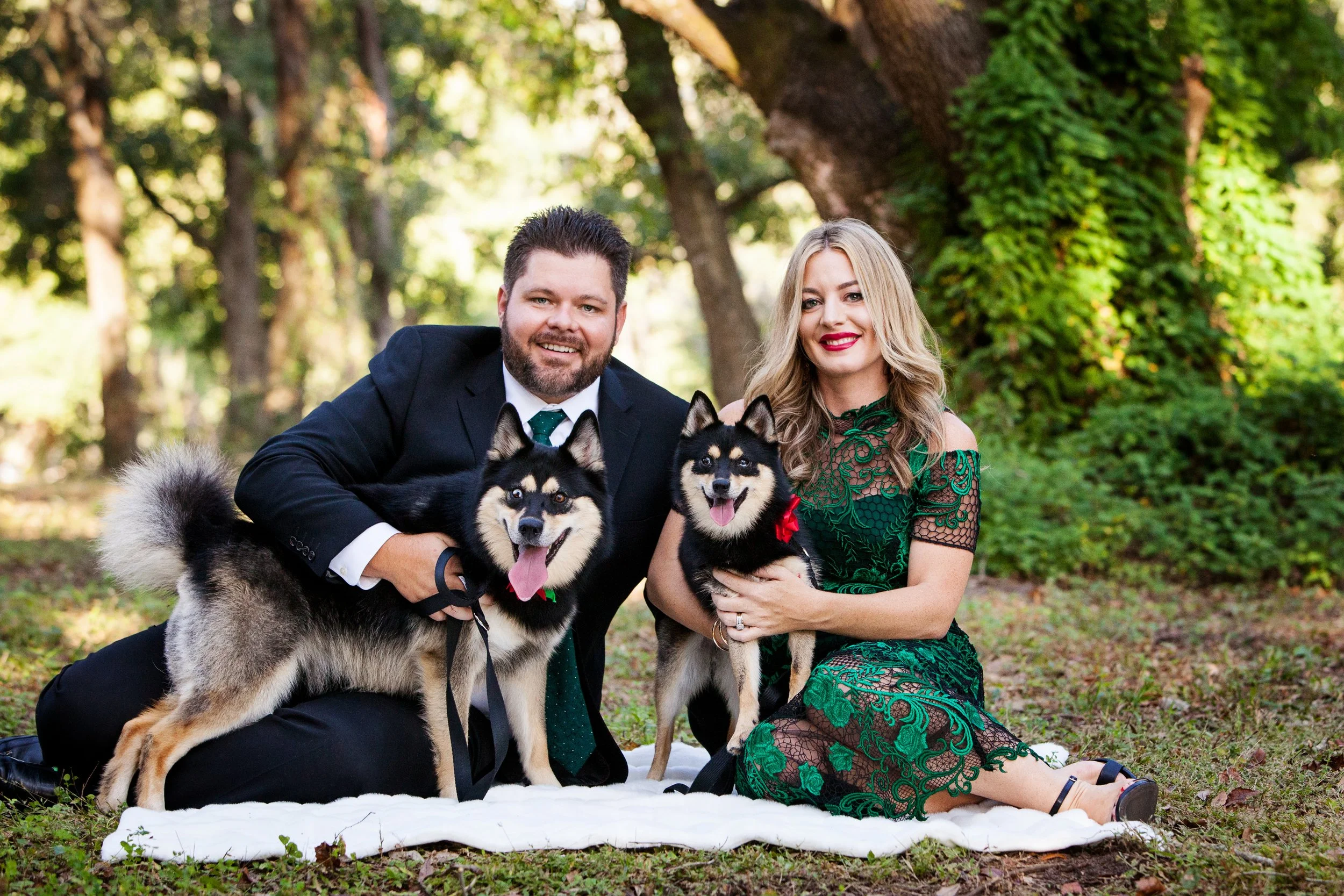 Lifestyle couple photography of a couple sitting on a blanket outdoors with their huskies beneath Florida trees