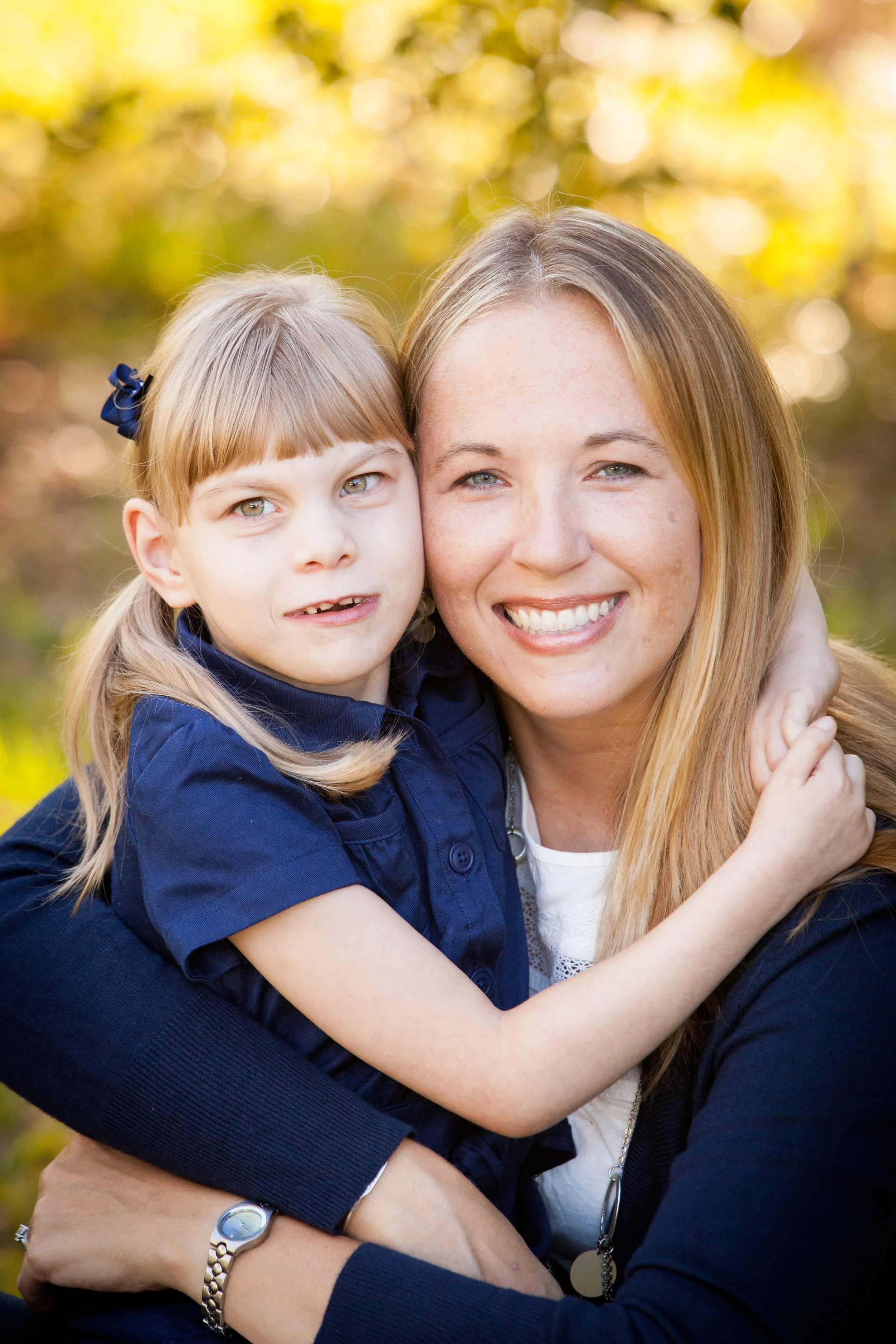 Fall family photography of a mother and daughter embracing beneath sunlit trees