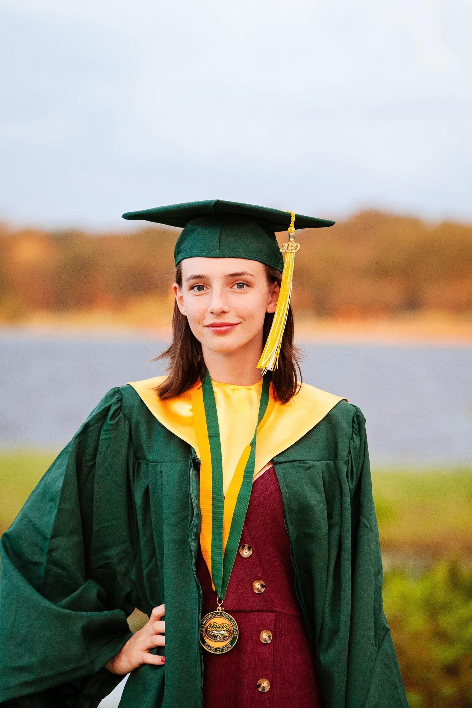 Senior graduation portrait of a woman in green cap and gown celebrating by a body of water in Florida, photographed by Lindsay Parks Photography