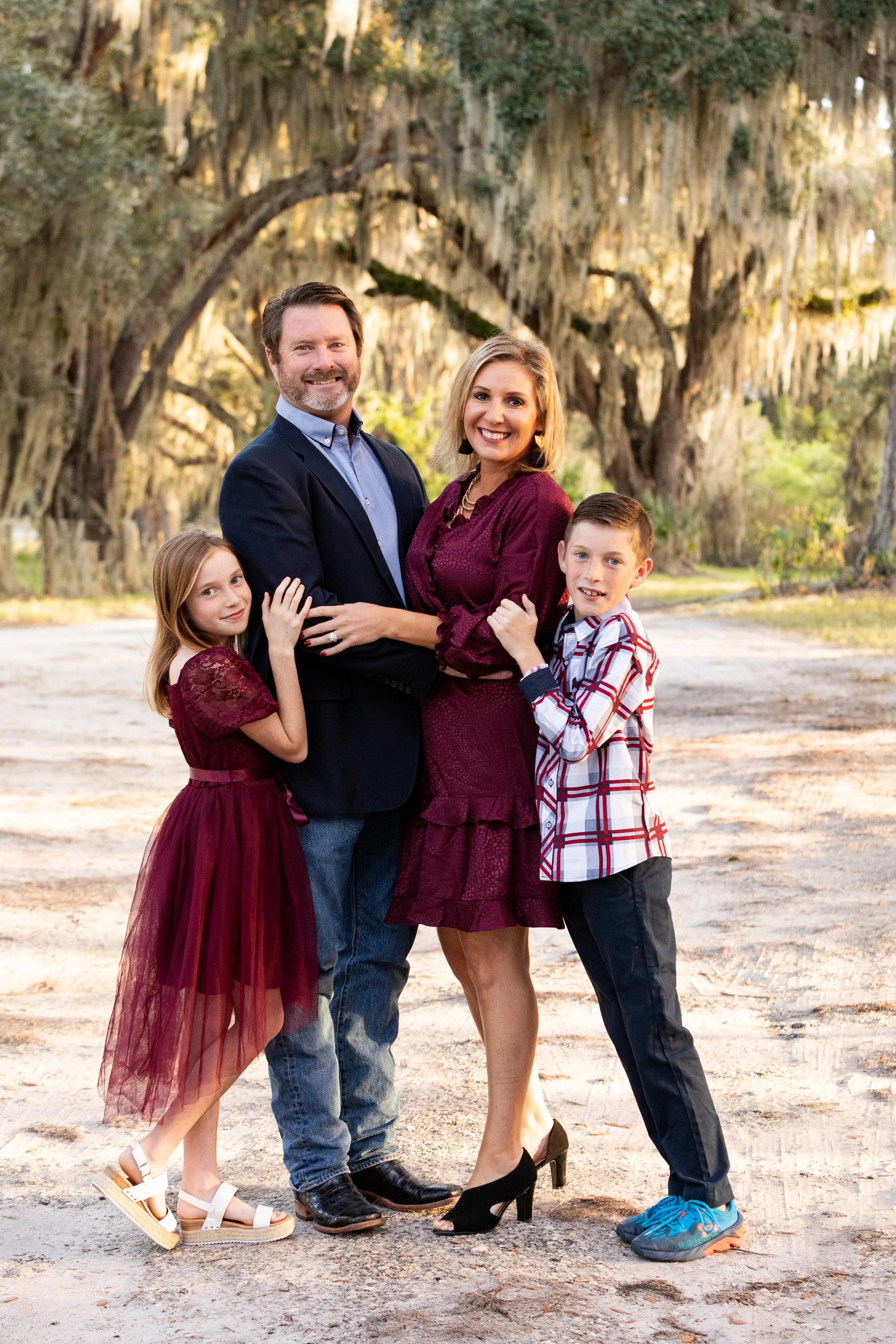 Outdoor family portrait of a family of four hugging beneath moss-covered trees in Florida 