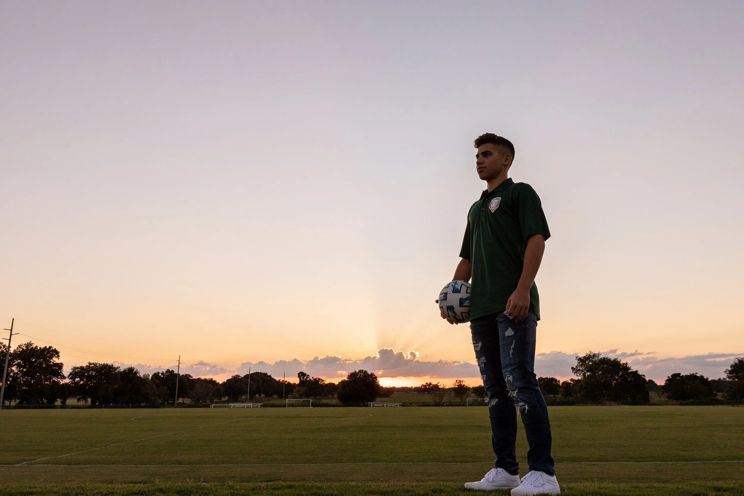 Senior sports portrait of a young man holding a soccer ball on an empty field at sunset in Florida, photographed by Lindsay Parks Photography