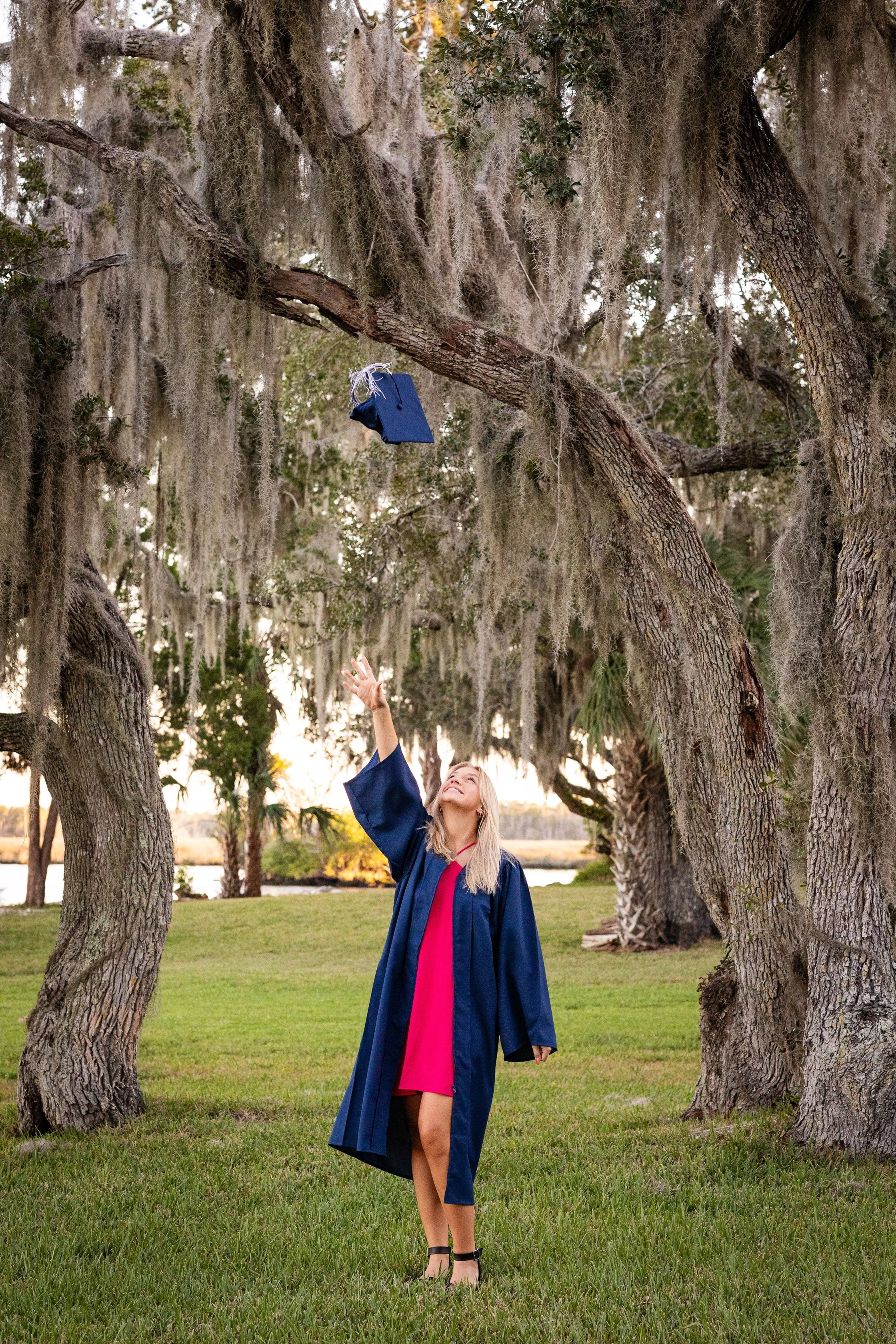 Graduation photography of a senior tossing her cap in the air beneath Spanish moss trees in Florida, photographed by Lindsay Parks Photography