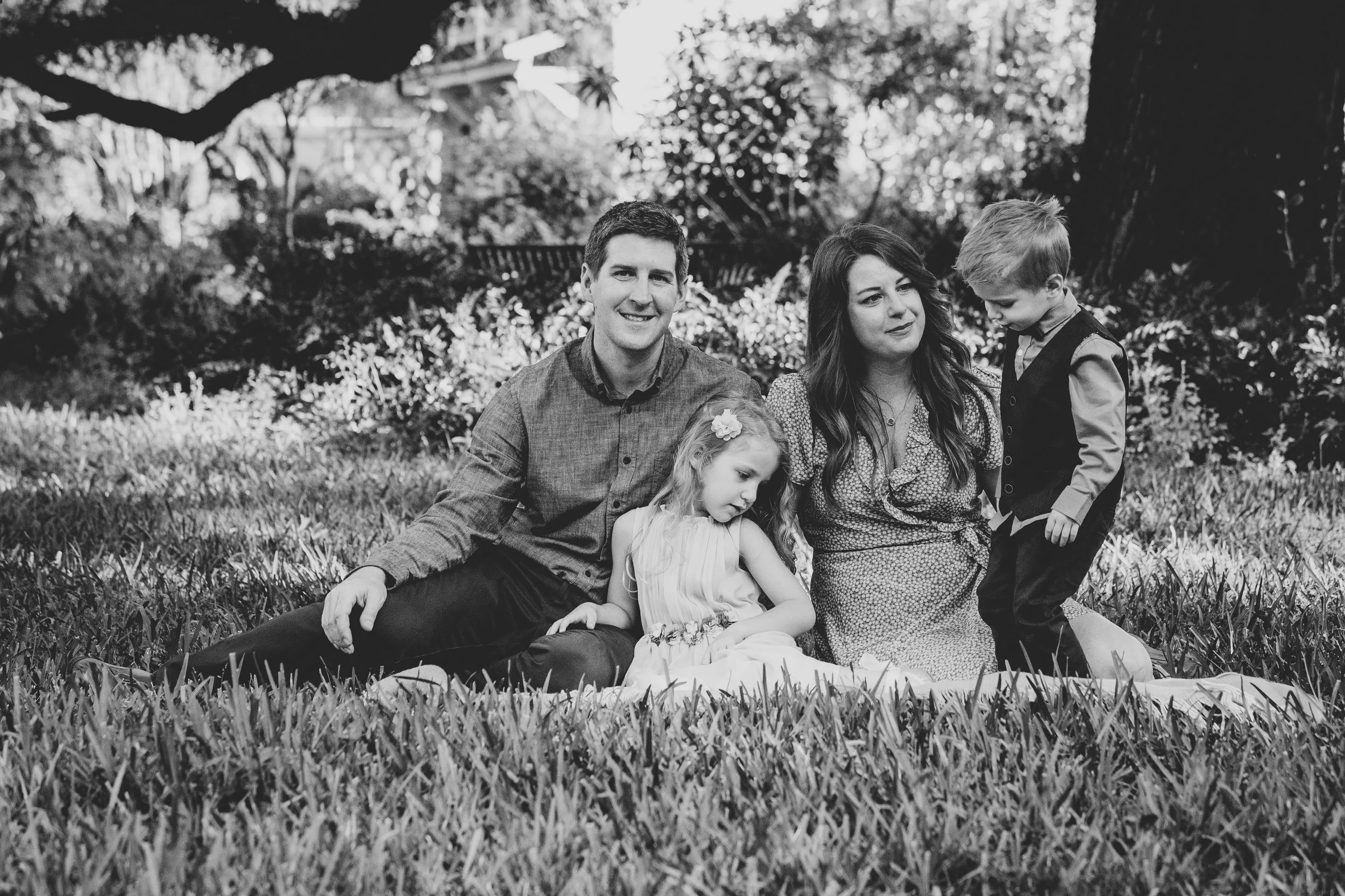 Black and white family portrait of a family of five sitting together on grass in a park