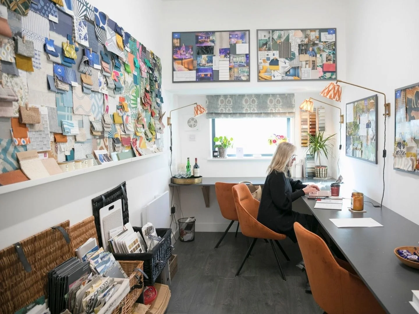 A woman working at a desk with colorful fabric samples and design boards on the walls of a bright, creatively decorated room.