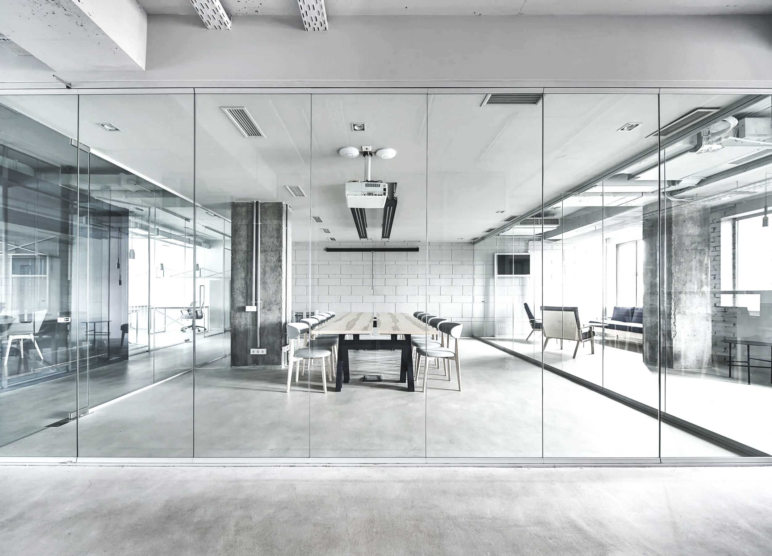 Modern conference room with glass walls, a long table, and chairs, illuminated by natural light from large windows.