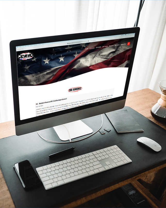 Computer monitor displaying a website with an American flag background and text related to the NBA schedule, placed on a wooden desk with a keyboard, mouse, notepad, and a glass of water.