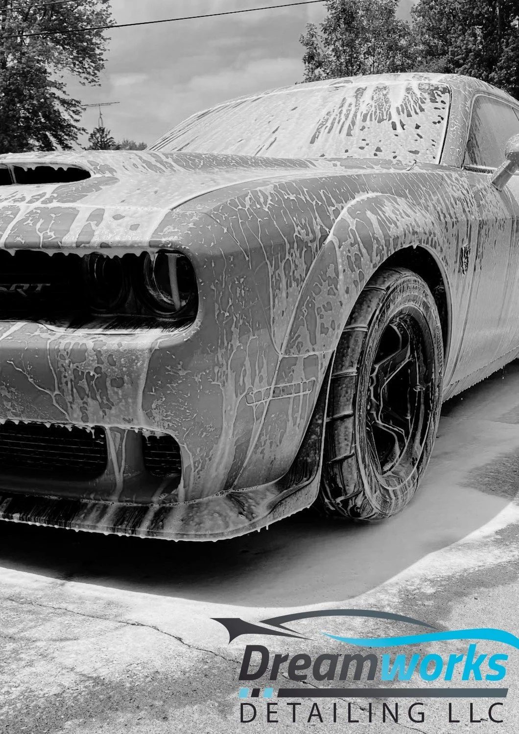 A car covered in soap suds during a car wash, with the logo 'Dreamworks Detailing LLC' at the bottom.