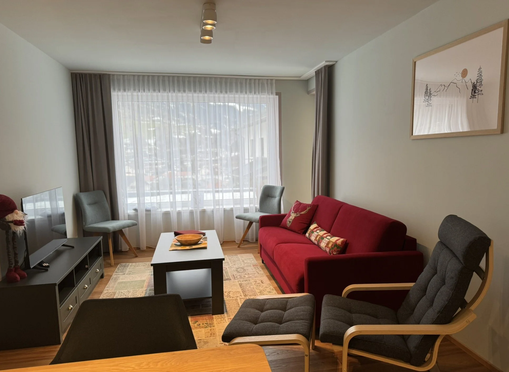 Wohnzimmer mit rotem Sofa,  Fernseher und Panoramafenster mit Talblick.