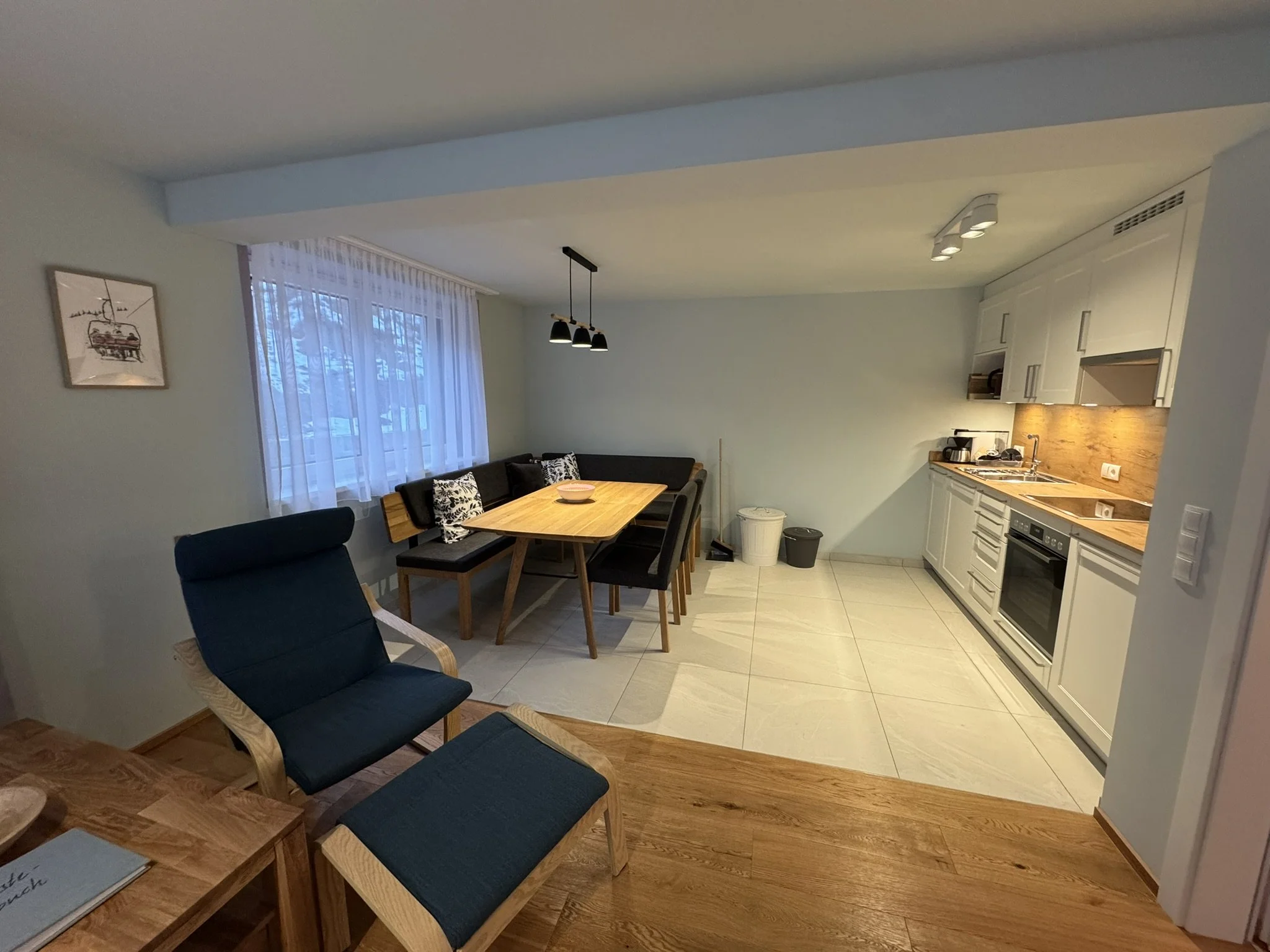 Offene Küche und Essbereich mit Eckbank, Fenster, Tisch und Stühlen. Wohnzimmer mit Sofa, Sessel, Tal- und Alpenpanorama.