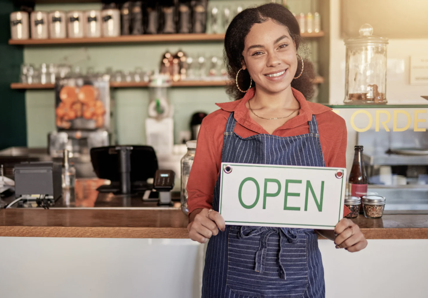 Woman holding a sign in a coffee shop that says Open