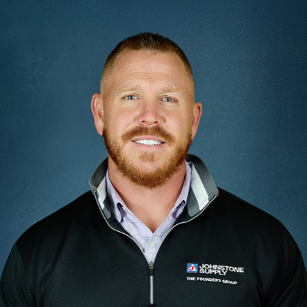 Portrait of a man with short hair, beard, and light skin, wearing a black jacket with the Johnstone Supply logo, against a blue background.