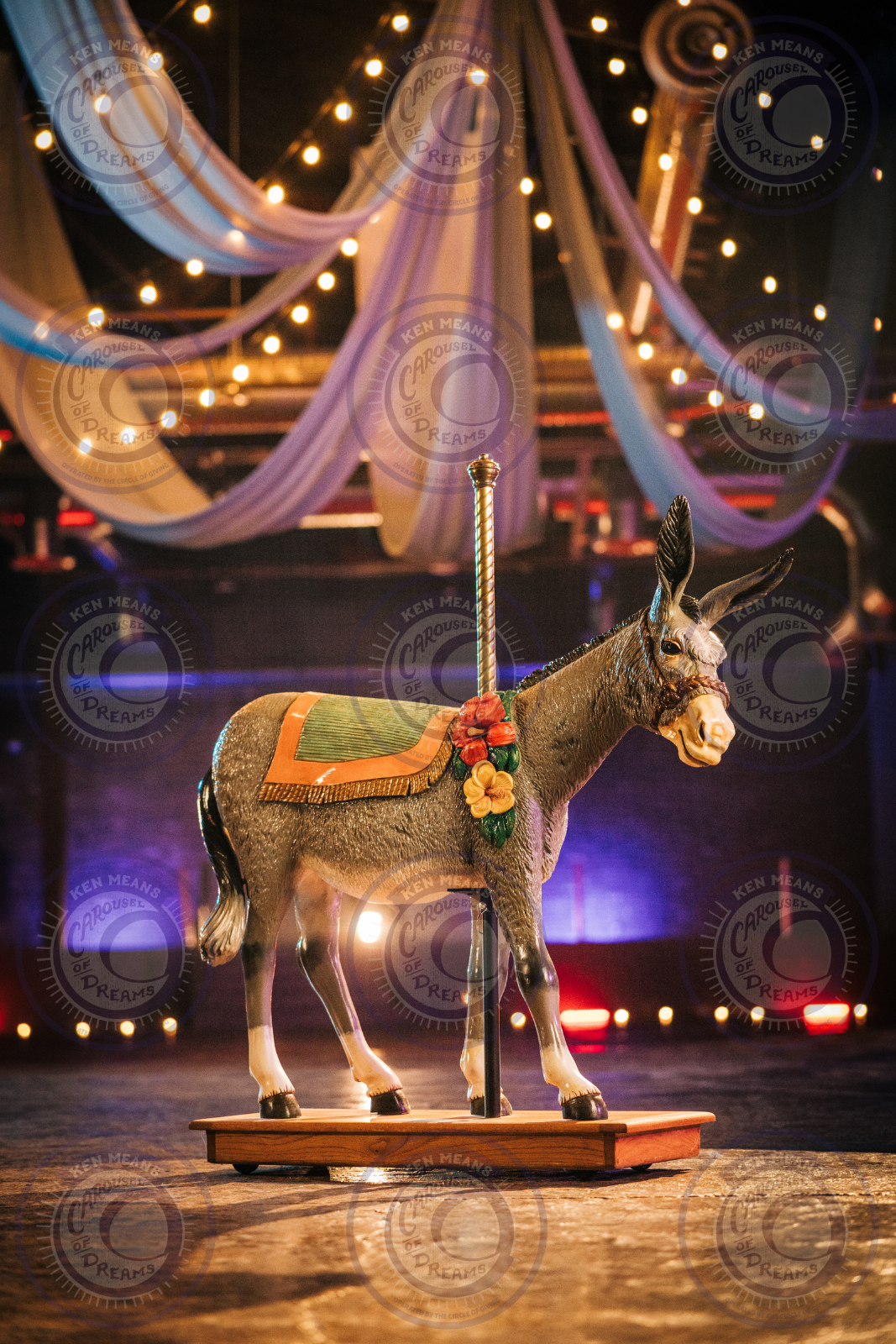 Decorative donkey carousel figure on wooden base with draped ceiling and lights