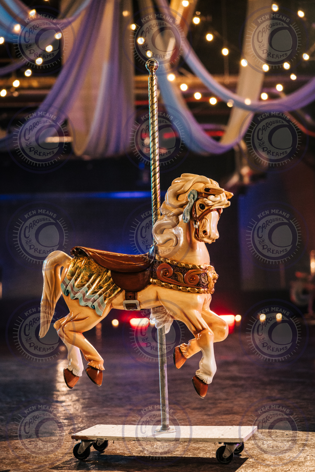 A vintage carousel horse on a wheeled platform with decorative lights and draped fabric in the background.