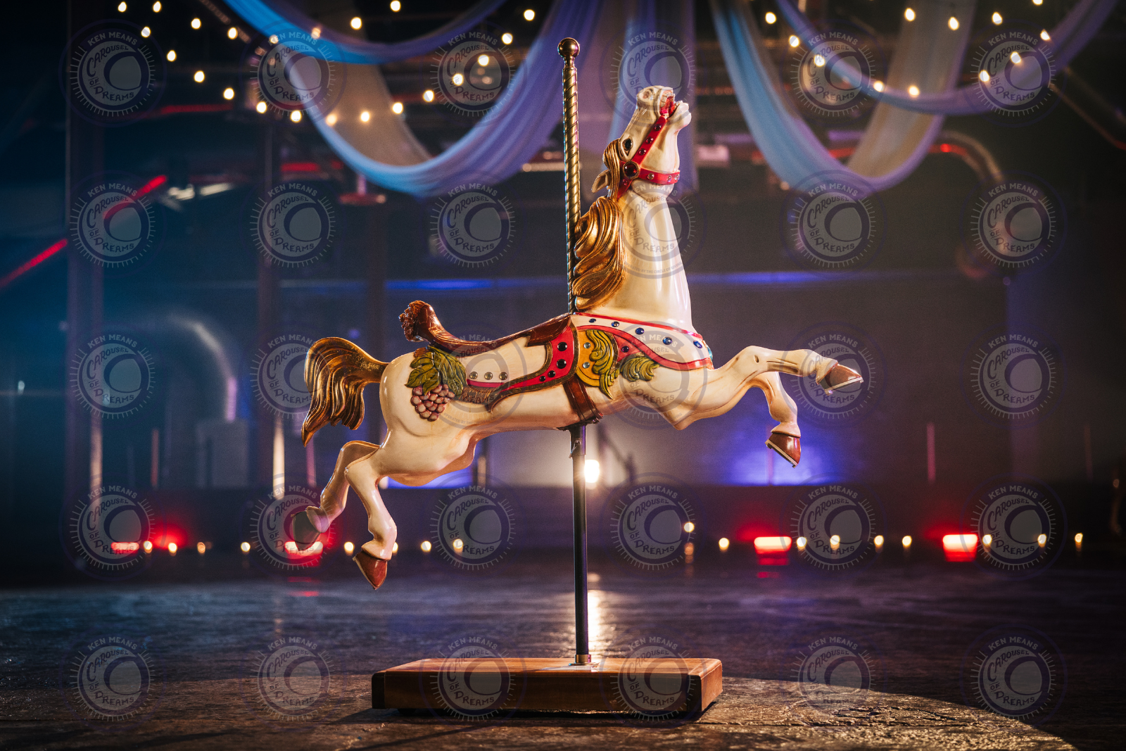 Decorative carousel horse under string lights in dimly lit room; blue and purple drapes hang above.