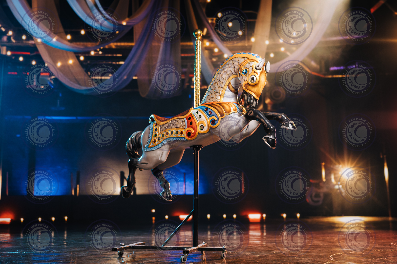 A colorful carousel horse on wheels in a dimly lit room with draped fabric and string lights in the background.