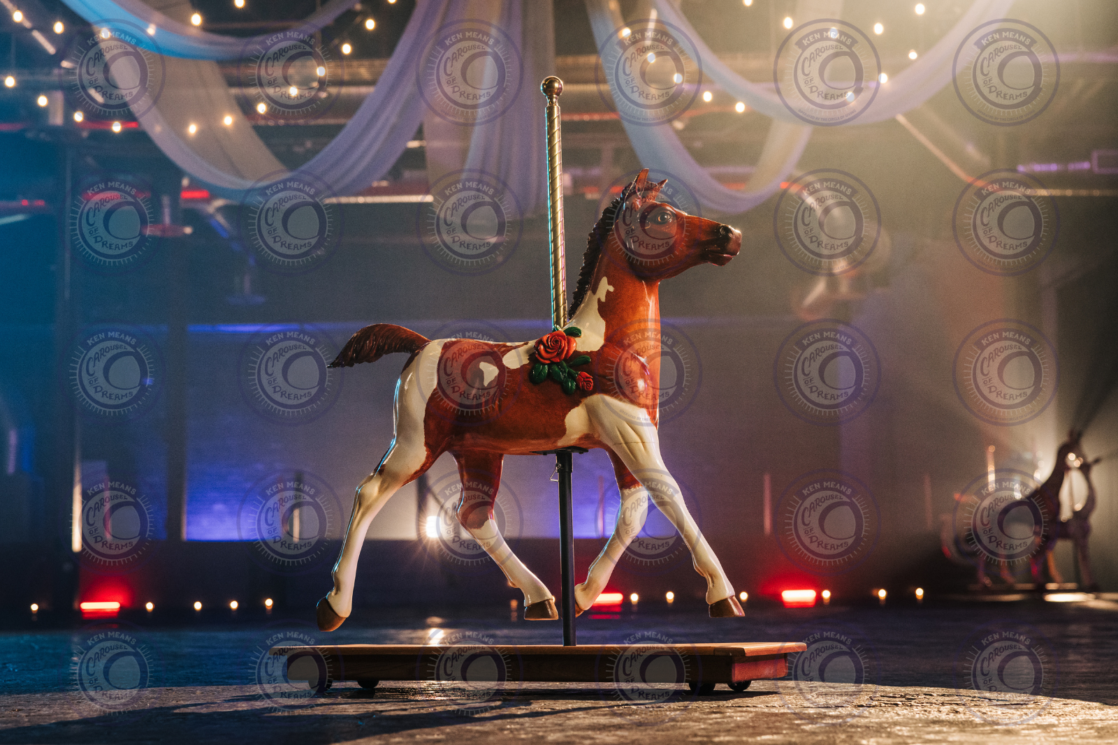A carousel horse with decorative roses indoors with ambient lighting and draped fabric ceiling.
