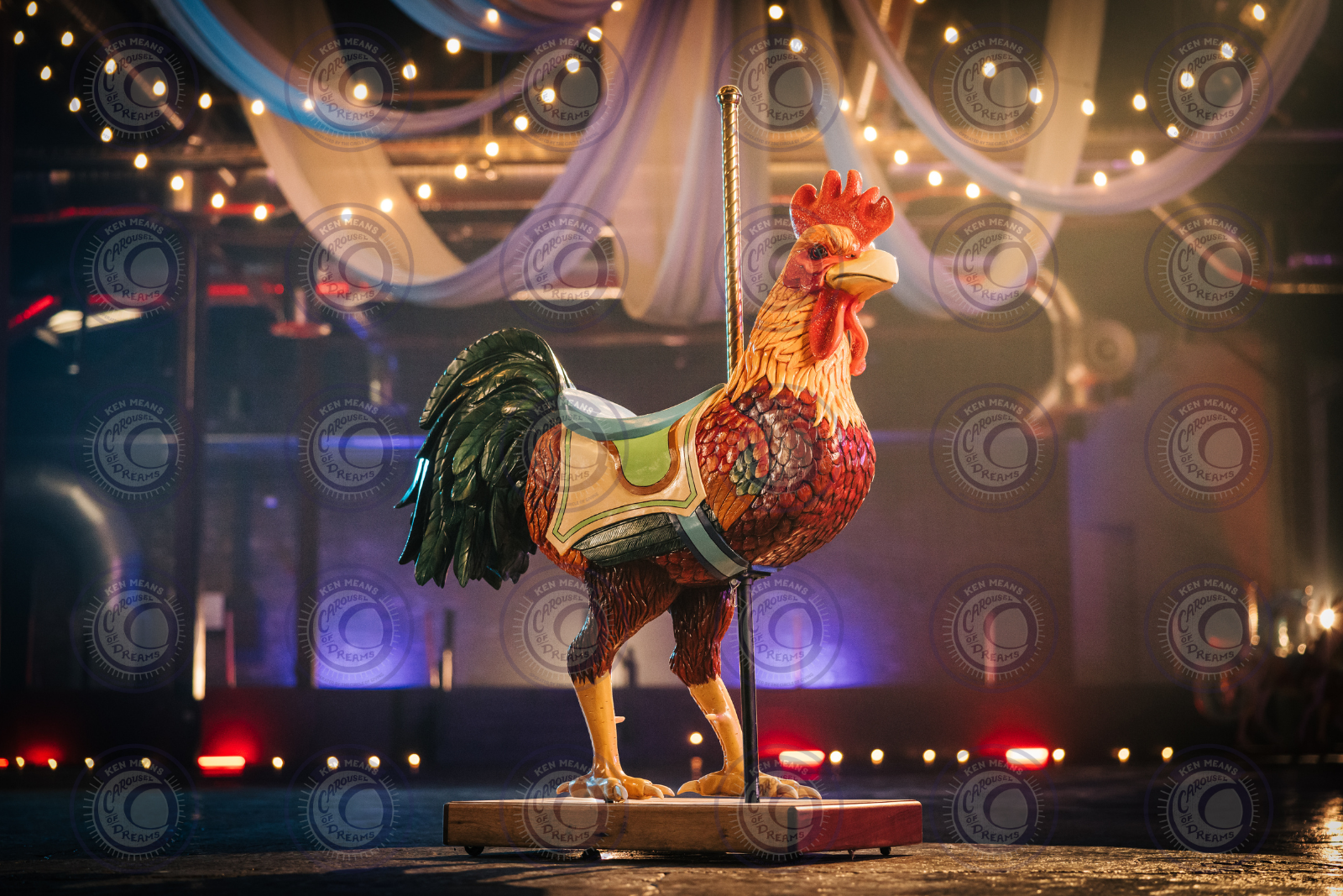 Colorful carousel rooster with a saddle, surrounded by hanging blue drapes and string lights in a dimly lit setting.