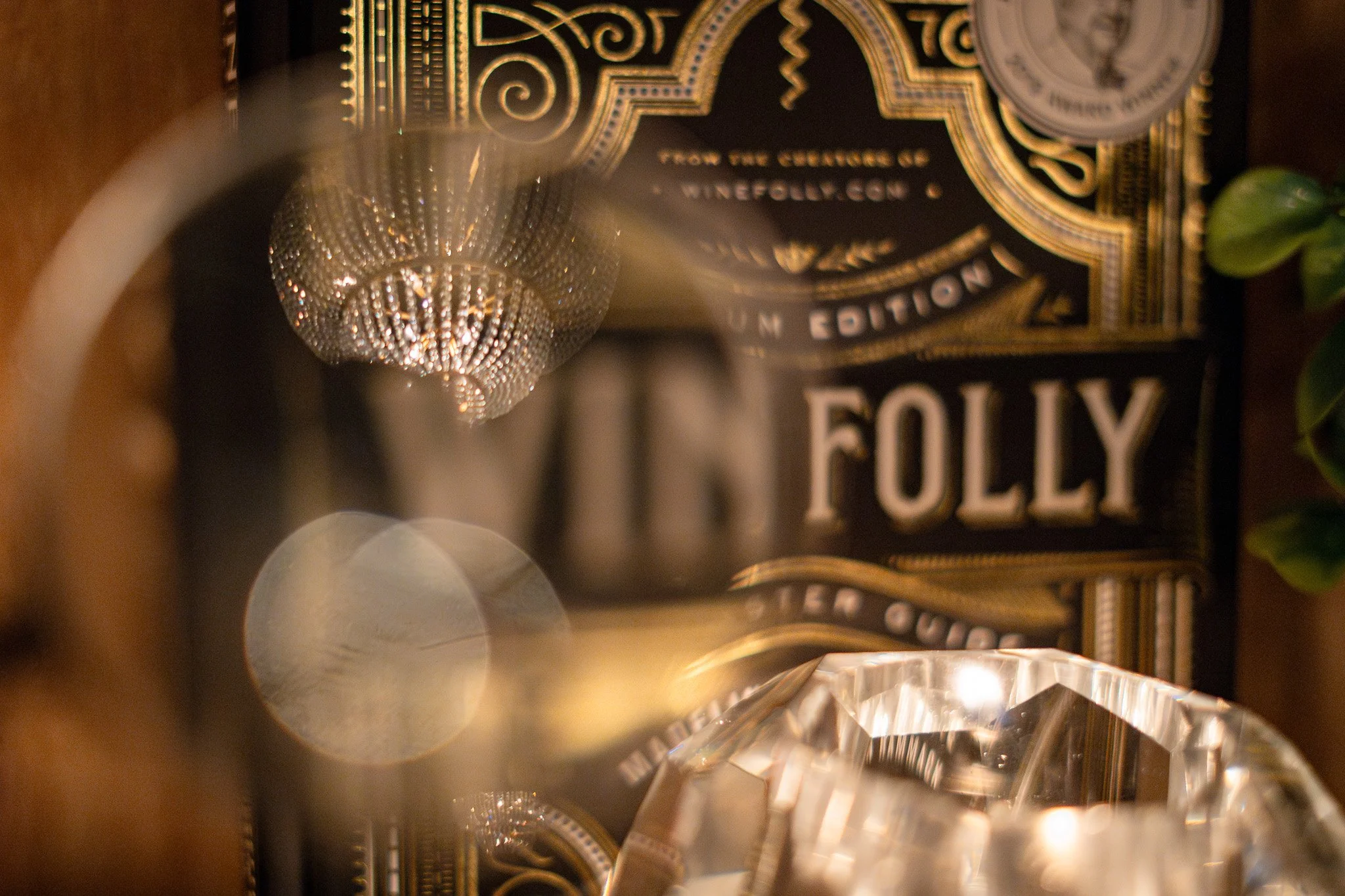 Close-up of a decorative box with gold accents and the word "FOLLY" on it, reflecting in crystal-like objects and a metal mesh sphere with small crystals inside.