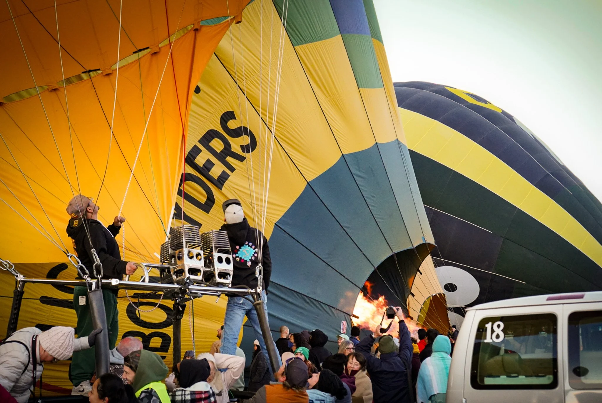 Hot air balloon preparing for flight with crowd gathered around, some taking pictures, during daytime.