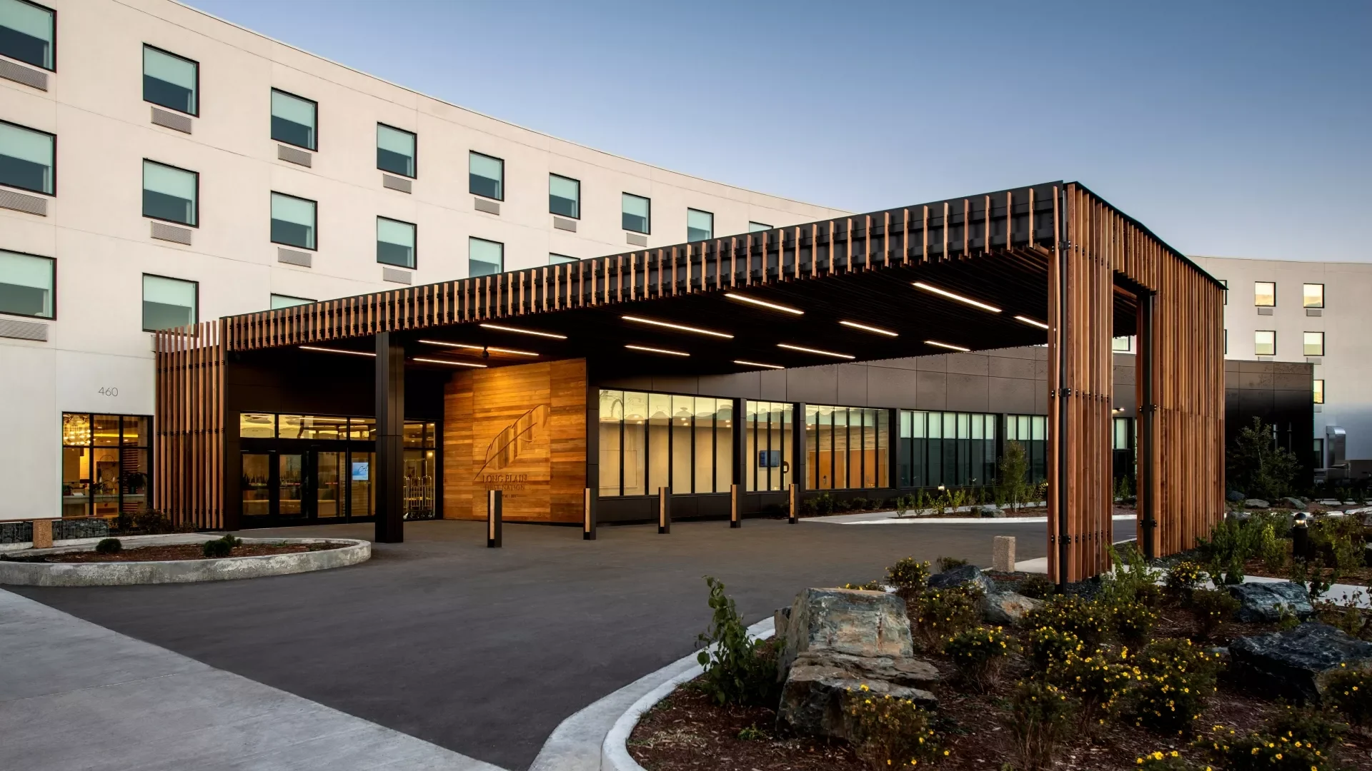 Modern hotel building with a wooden entrance canopy and landscaping in front.