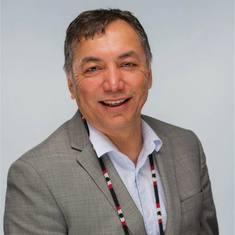A man wearing a gray suit and white shirt, smiling, against a plain background.
