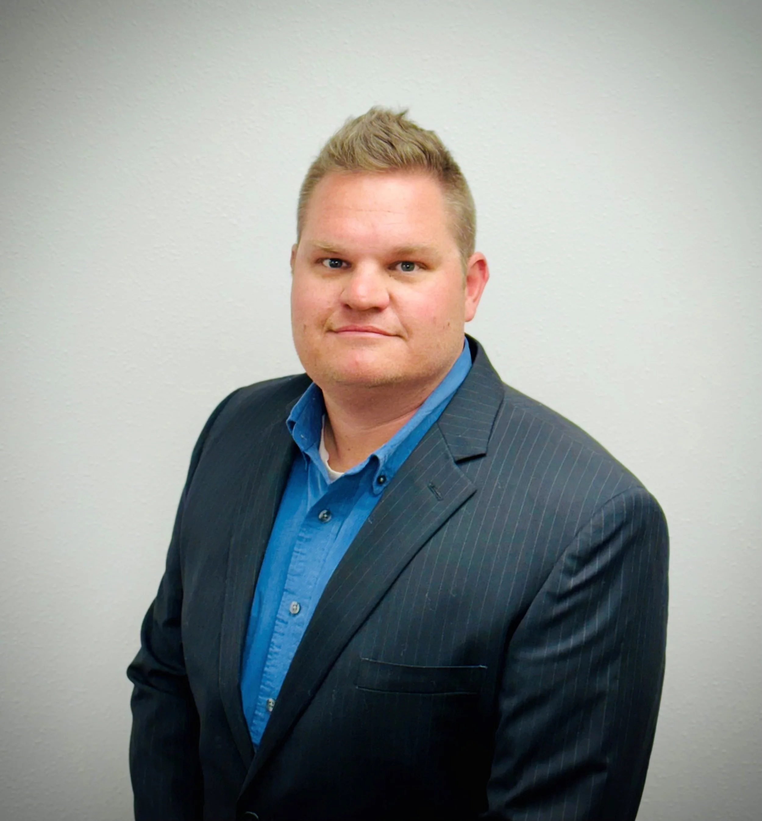 Man in a suit and blue shirt posing against a plain background.