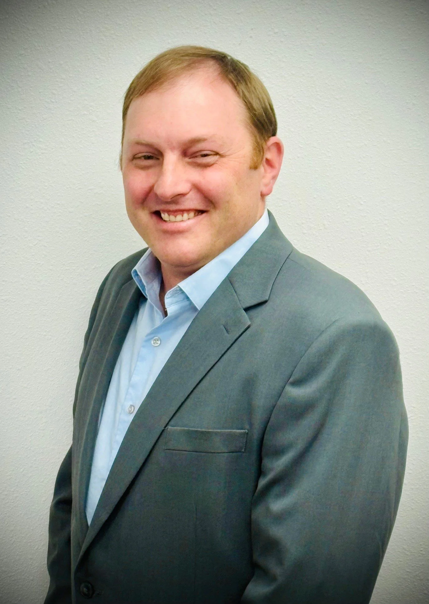 Man in a suit and blue shirt posing against a plain background.