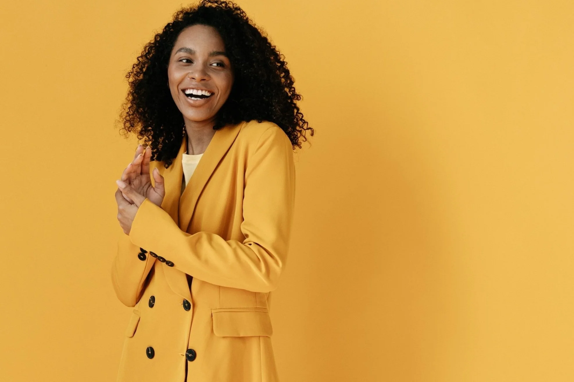 Smiling person in yellow blazer against yellow background.