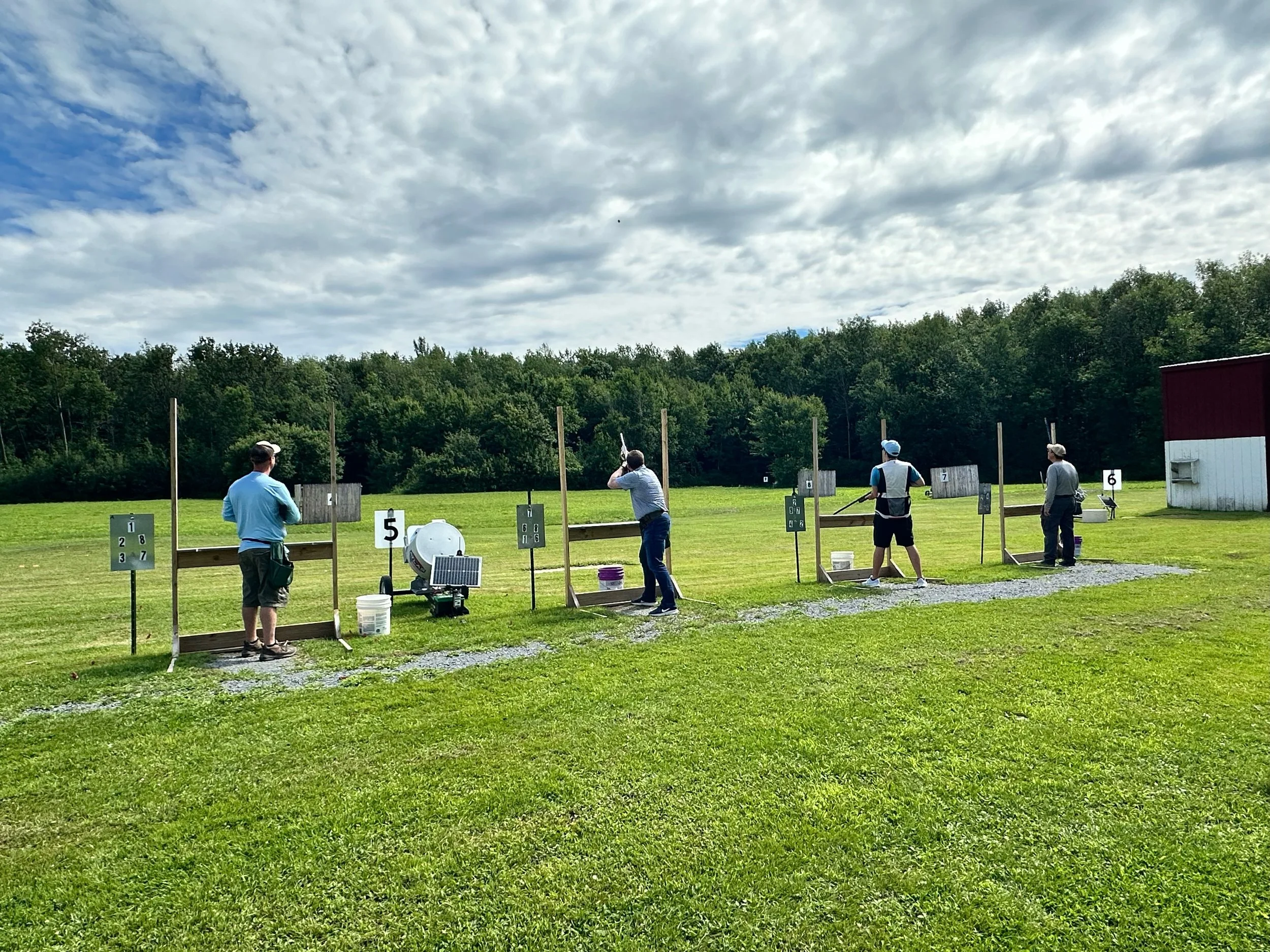 Four people practicing shot put at an outdoor range, with targets in the background and a cloudy sky overhead.